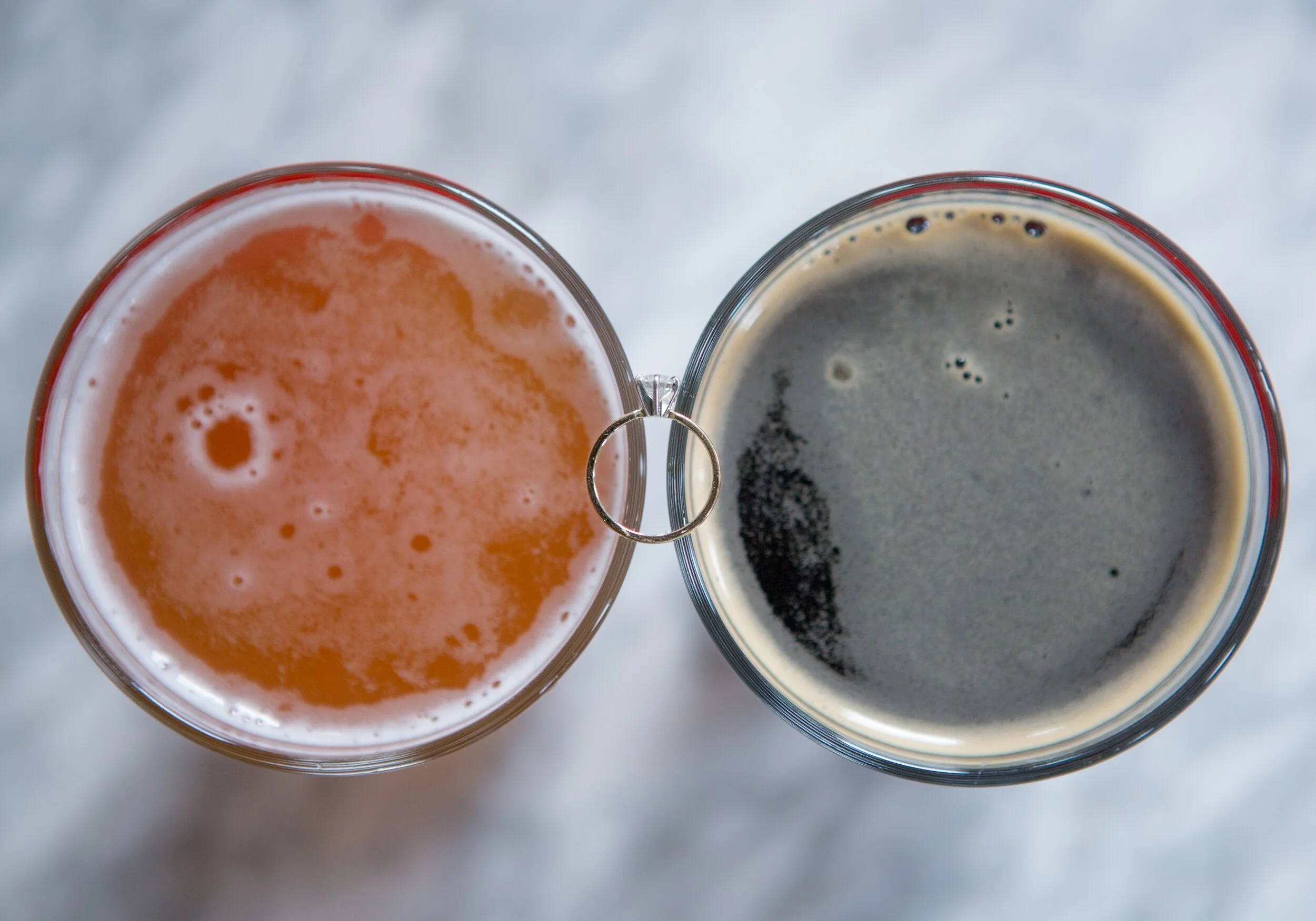 Top view of two glasses of beer on a white surface, connected by a metal ring handle.