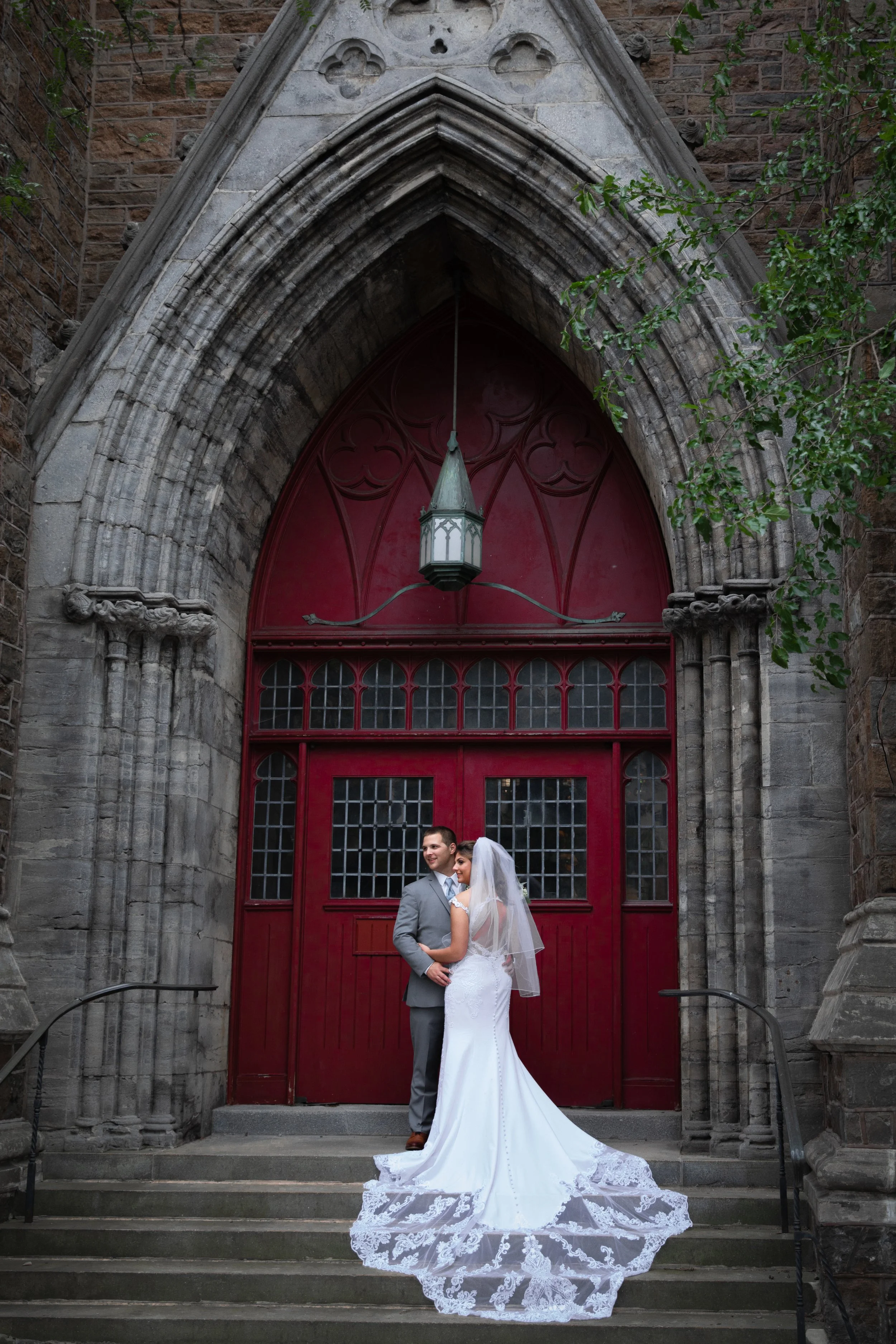 A newlywed couple is standing on the steps of a church in Downtown Utica NY 
