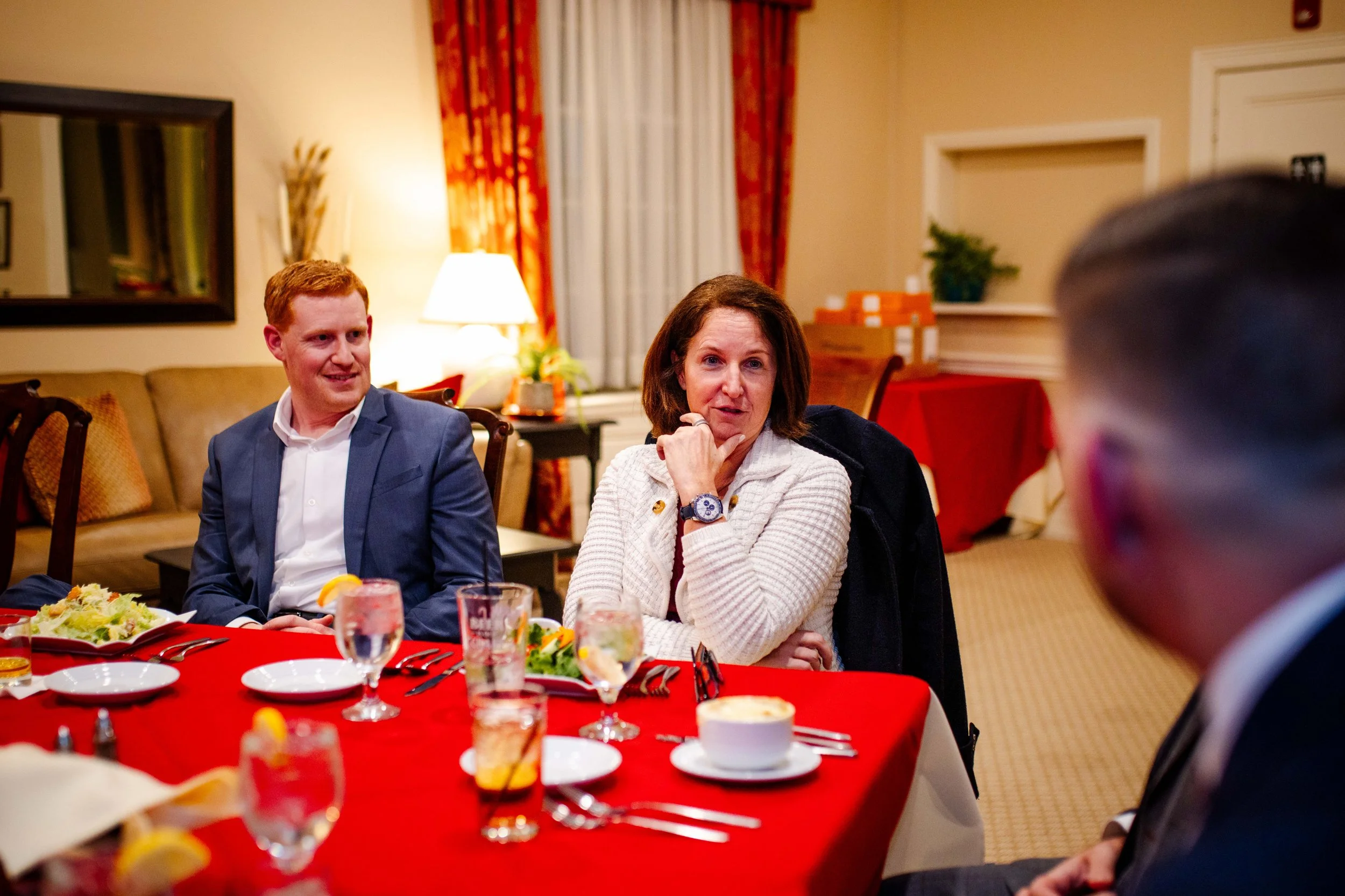 People sitting at a dinner table with food and drinks in a decorated room.