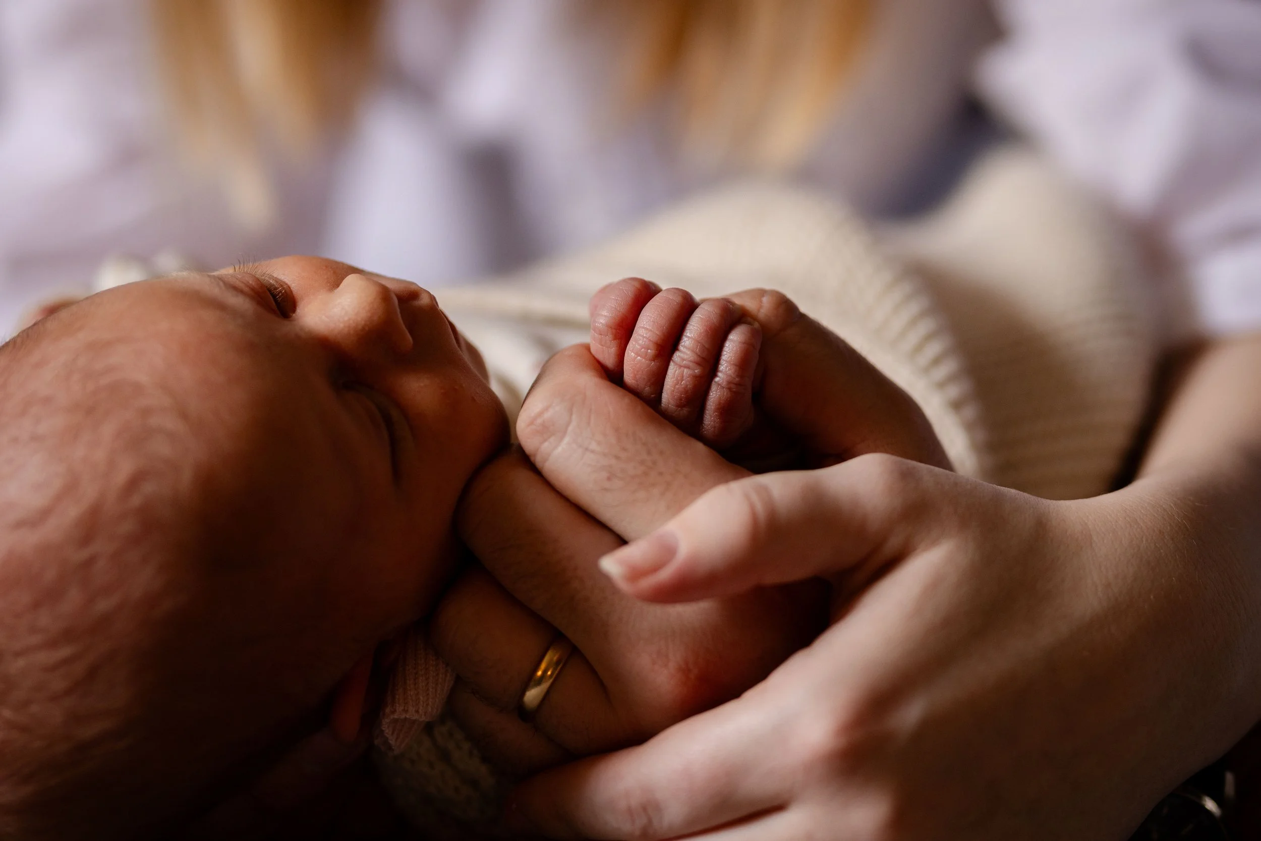 Close-up of a newborn baby's face and hand holding an adult's finger in a tender moment.