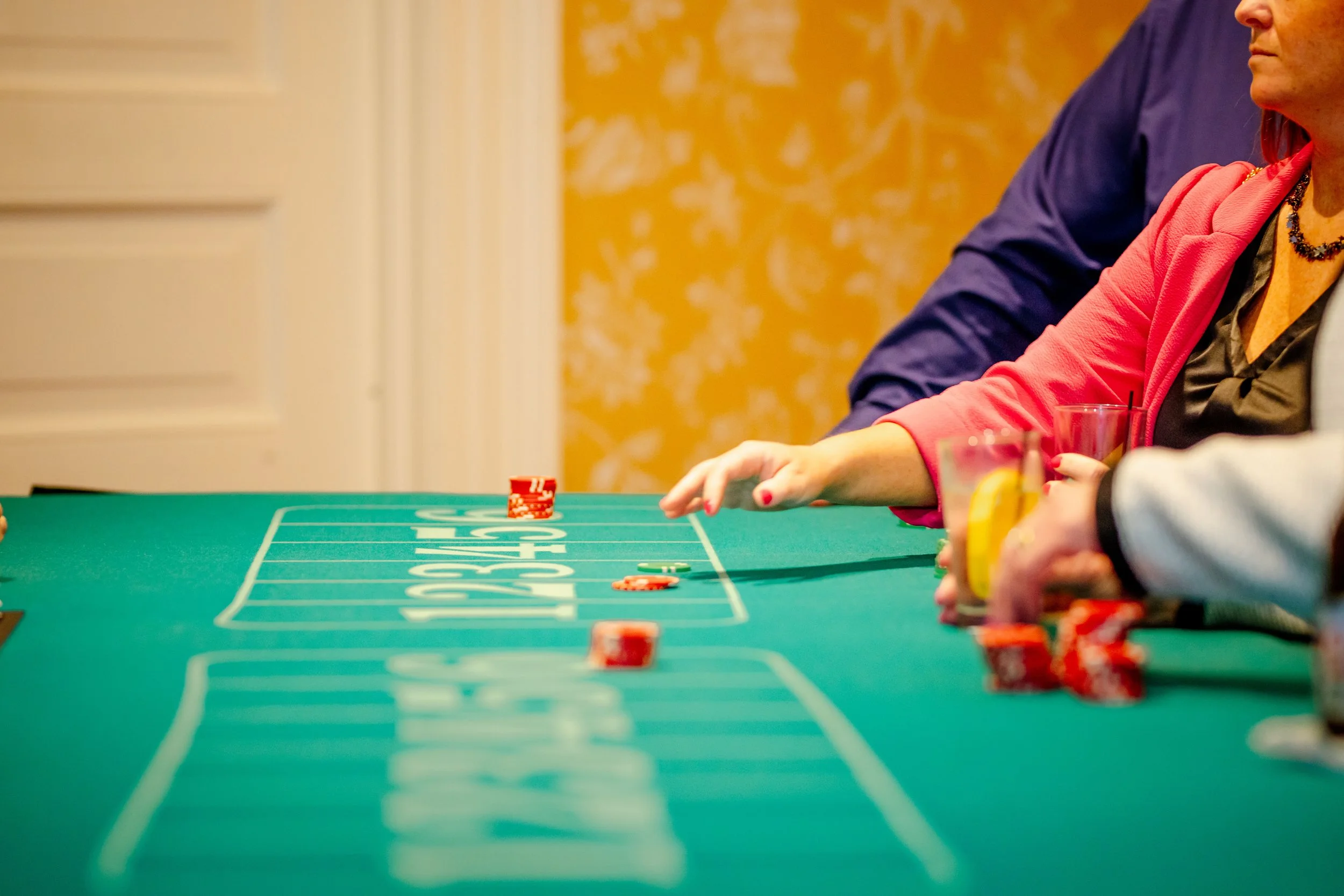 People playing casino craps game at a green table, with chips and drinks nearby.