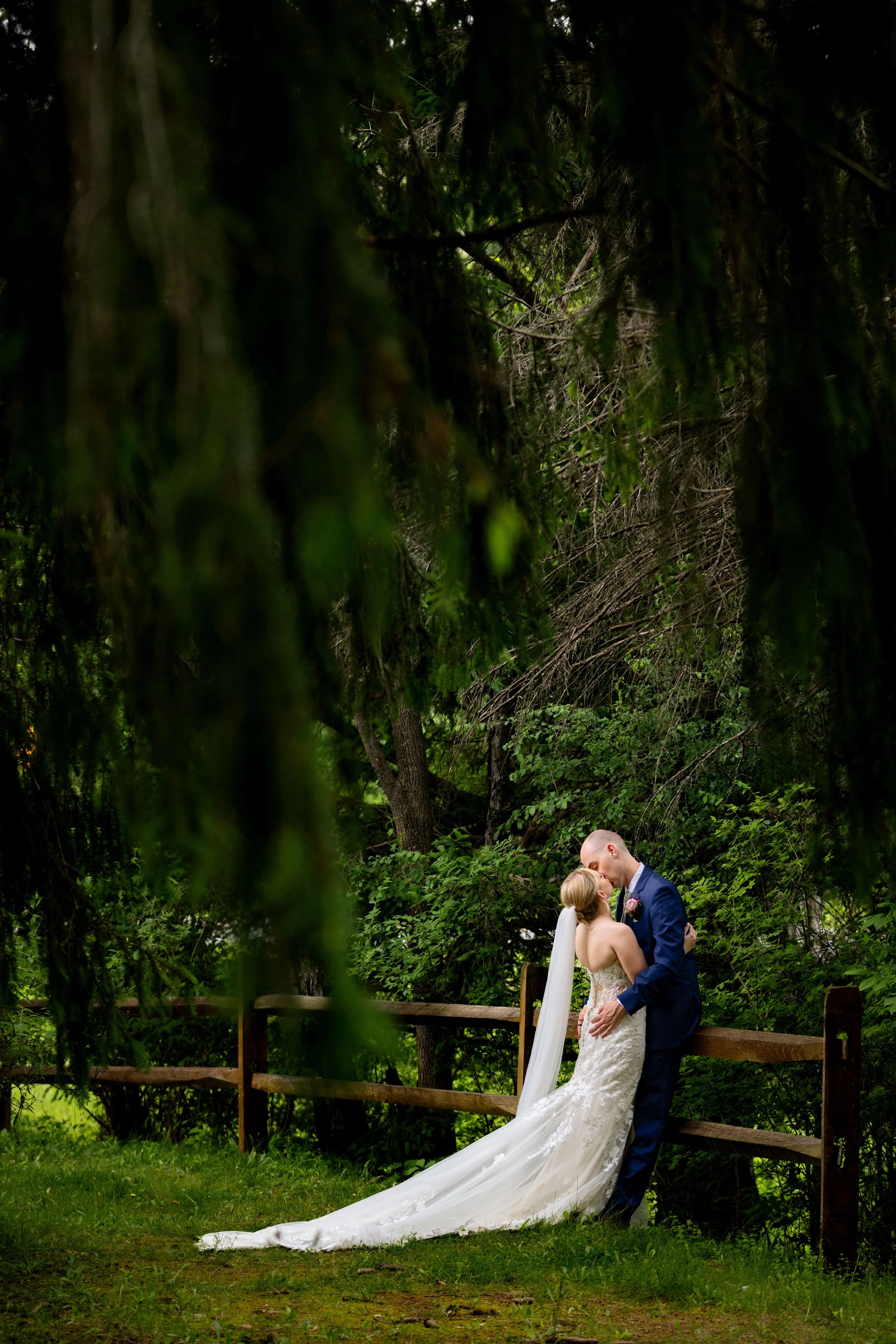 A bride and groom sharing a kiss outdoors in a wooded area on their wedding day.