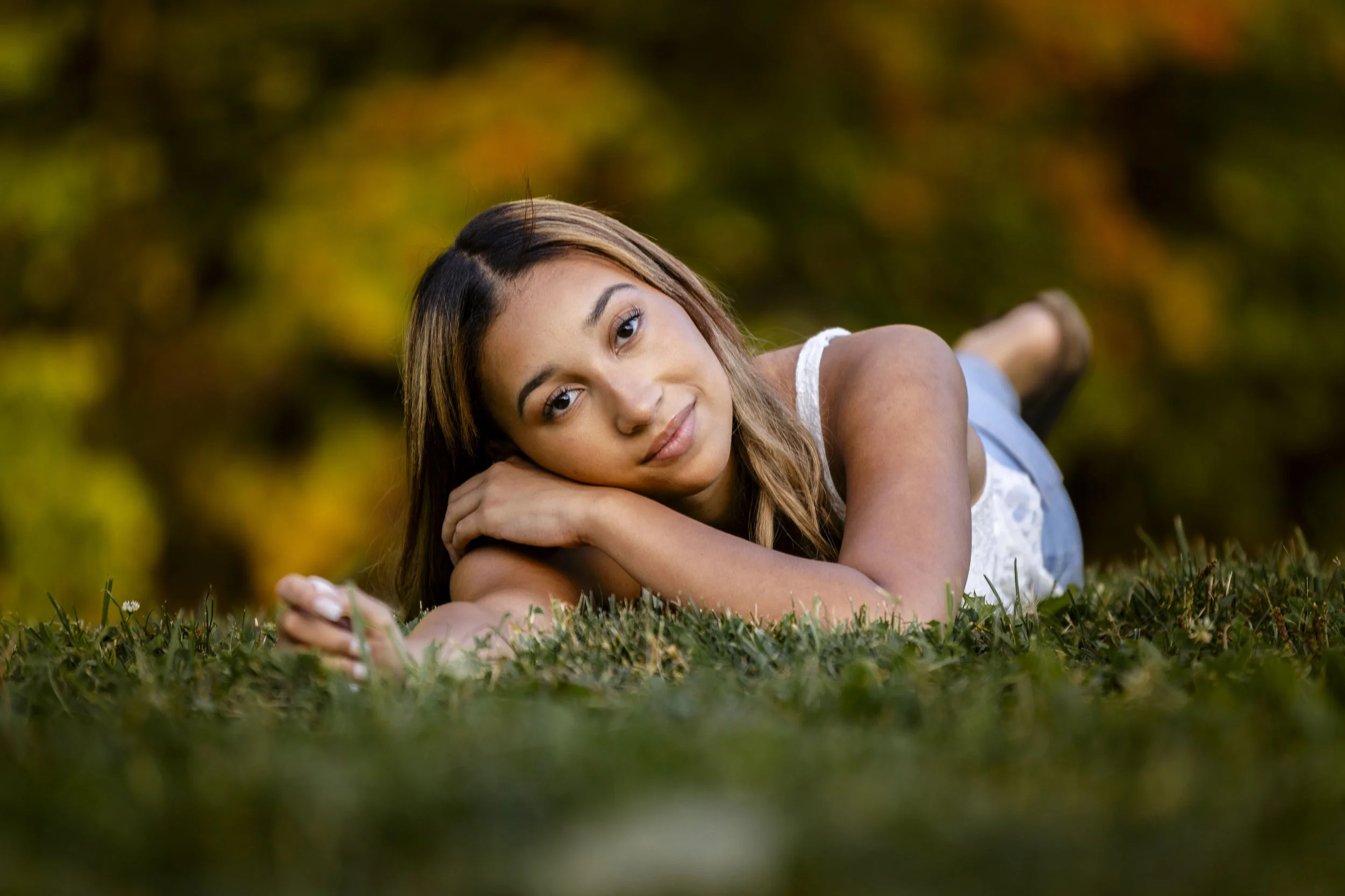 A high school senior is laying on the ground of Proctor Park while getting her photo taken 