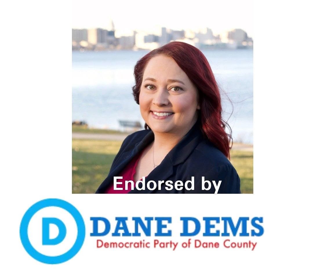 Smiling woman with red hair, wearing navy blazer in front of Lake Monona