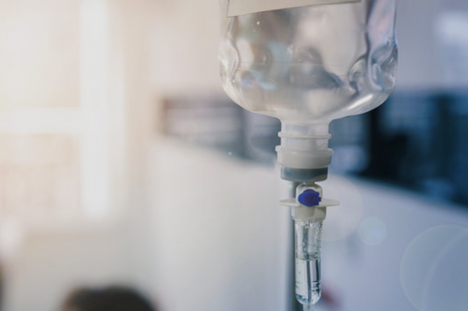 A close-up of a hospital IV drip with clear liquid, hanging in a medical setting.