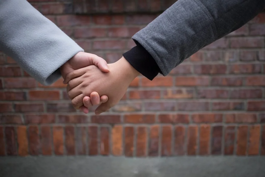 Two people shaking hands in front of a brick wall.