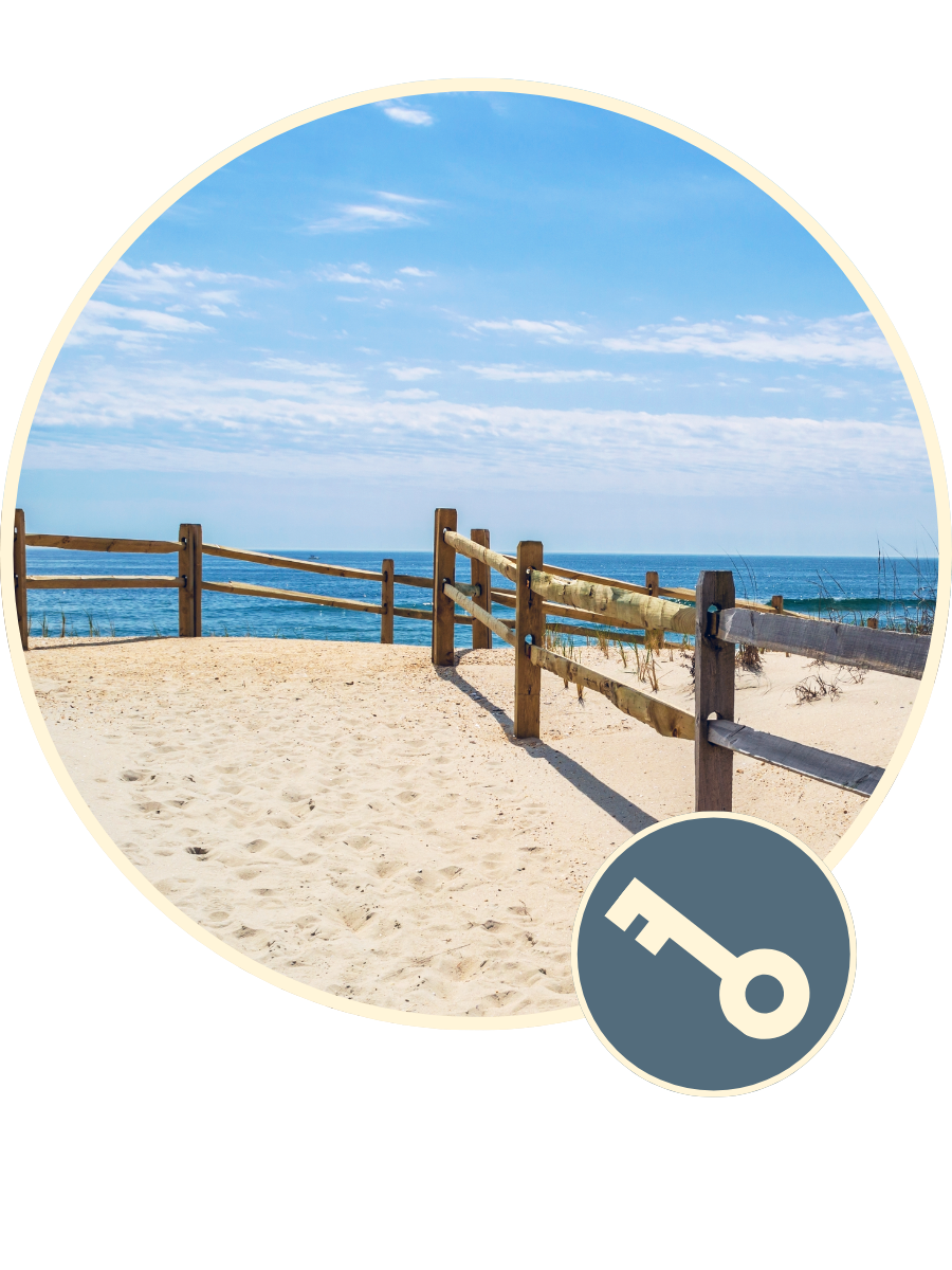 Beach with sandy shore, wooden fence, blue sky, and ocean in the background.