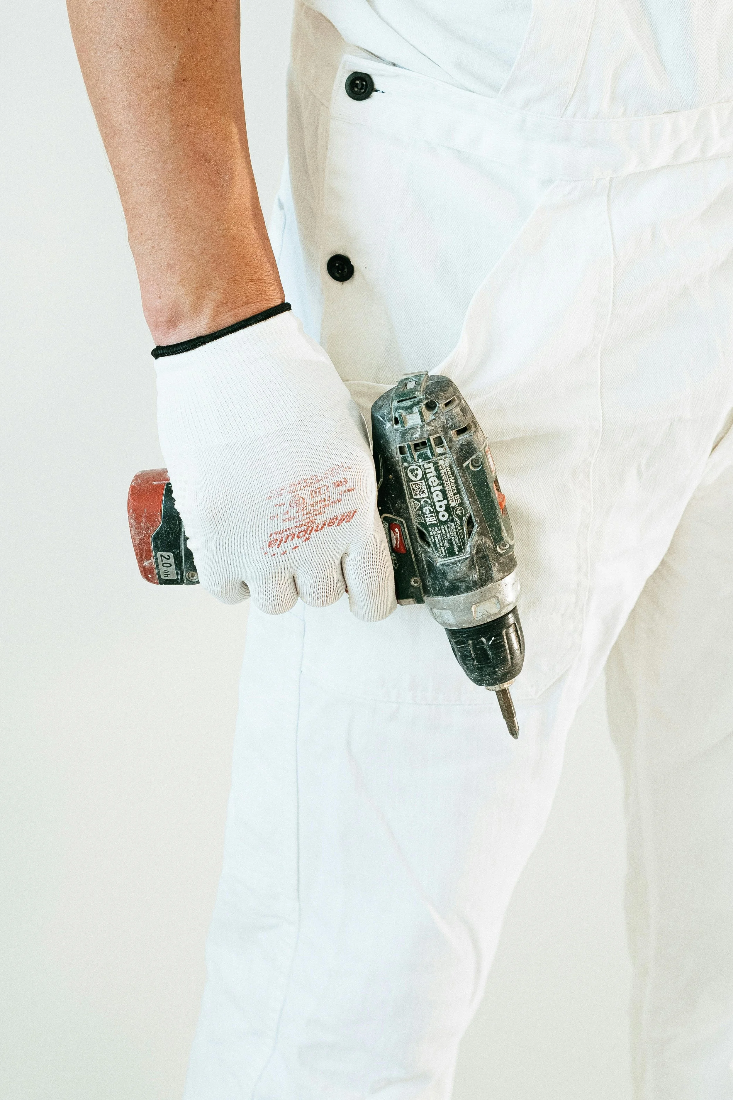 Person wearing white work gloves and white overalls holding a power drill.