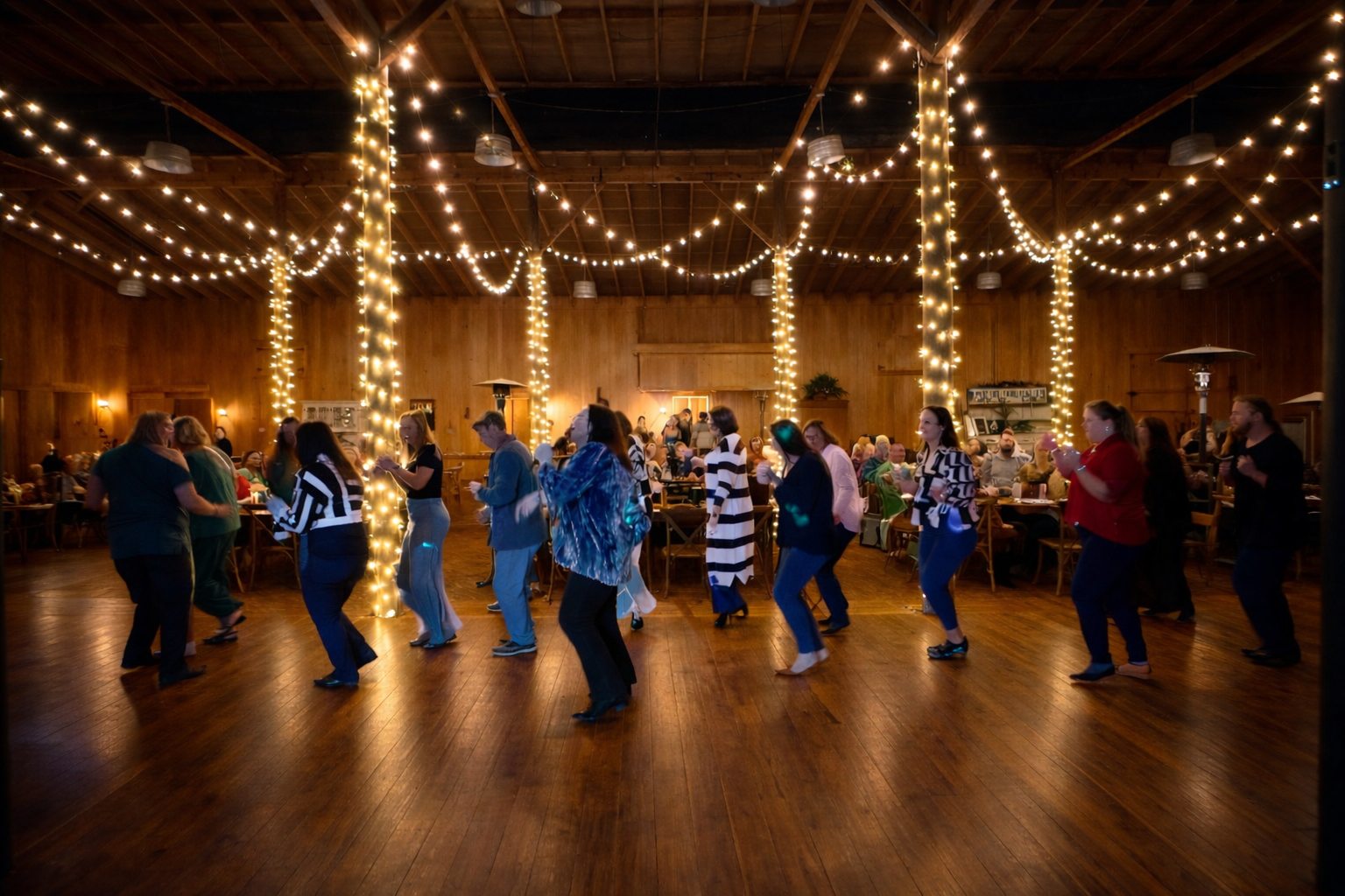 People dancing in a wooden-ceiling event space decorated with string lights.