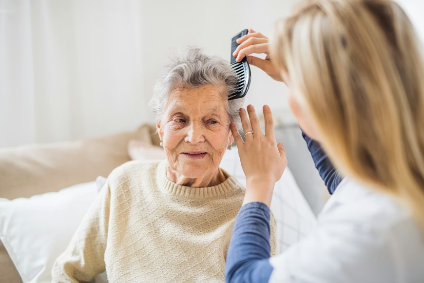 A young woman combing an elderly woman's gray hair in a bright room.
