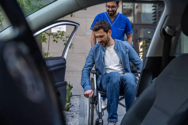 A man in a wheelchair being assisted by a healthcare professional, viewed from inside a car