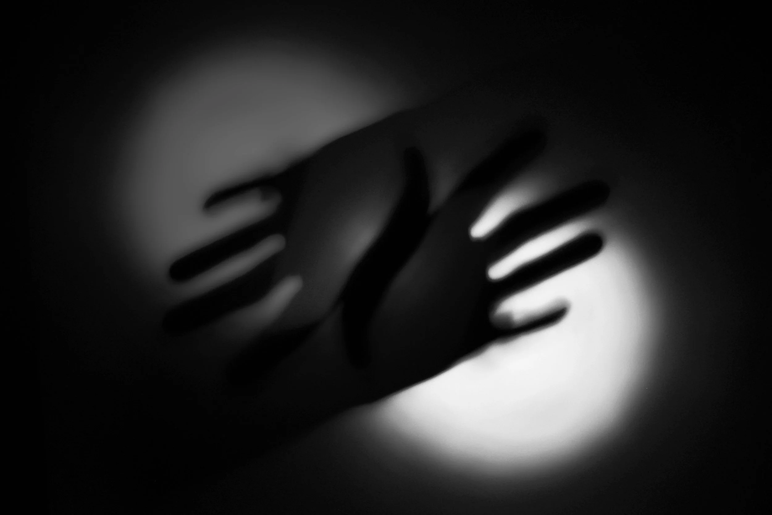 Photo of 2 hands showing in a silhouette. the hands are crossing, and in the background there are 2 circles of dim light.