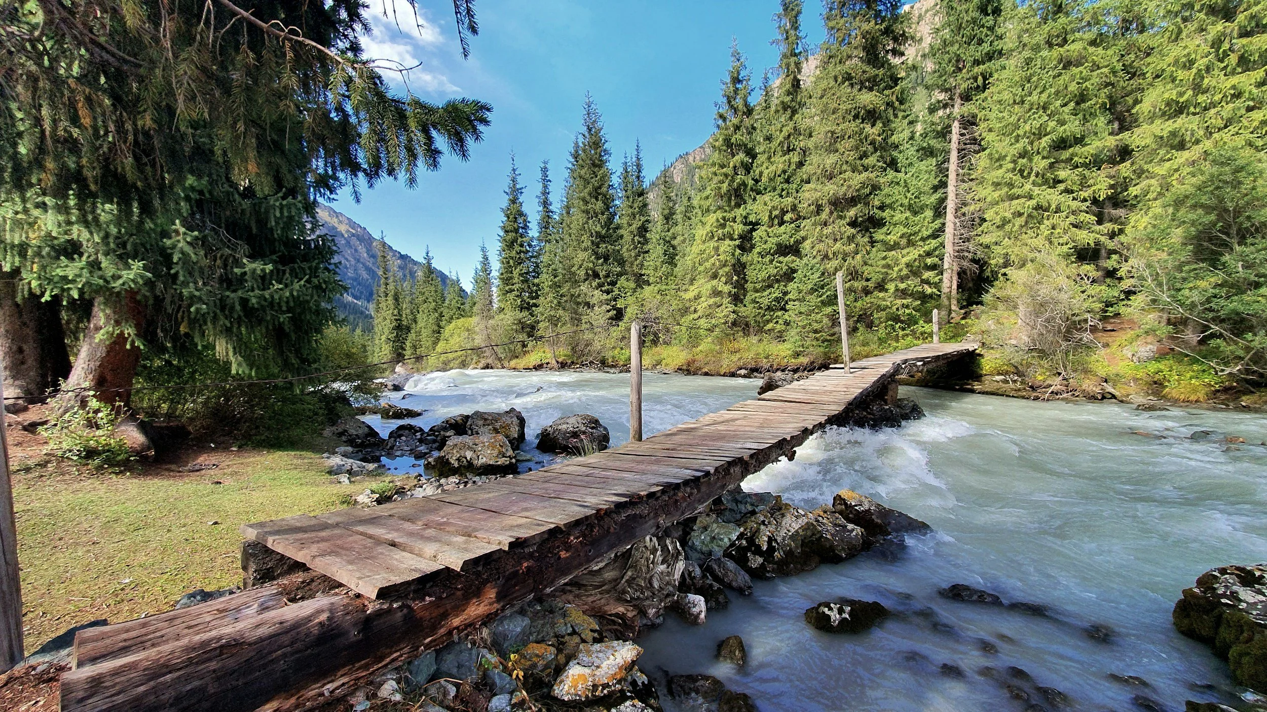 Kyrgyzstan freshwater river in the valleys during a sunny summer day. Wooden bridge over water.