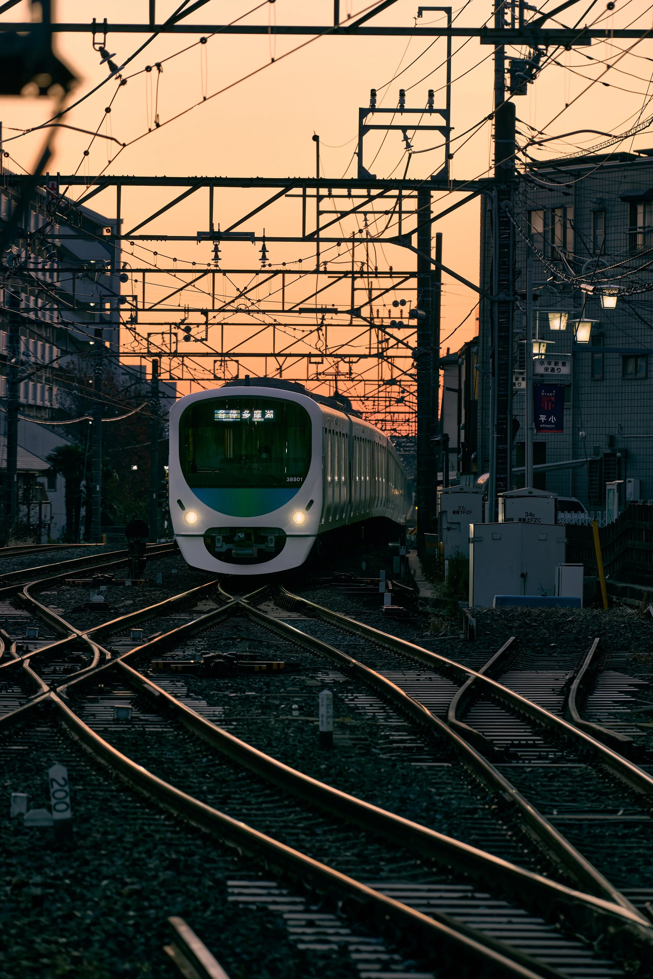 夕暮れ時の都市の鉄道線路を走る白い電車の写真