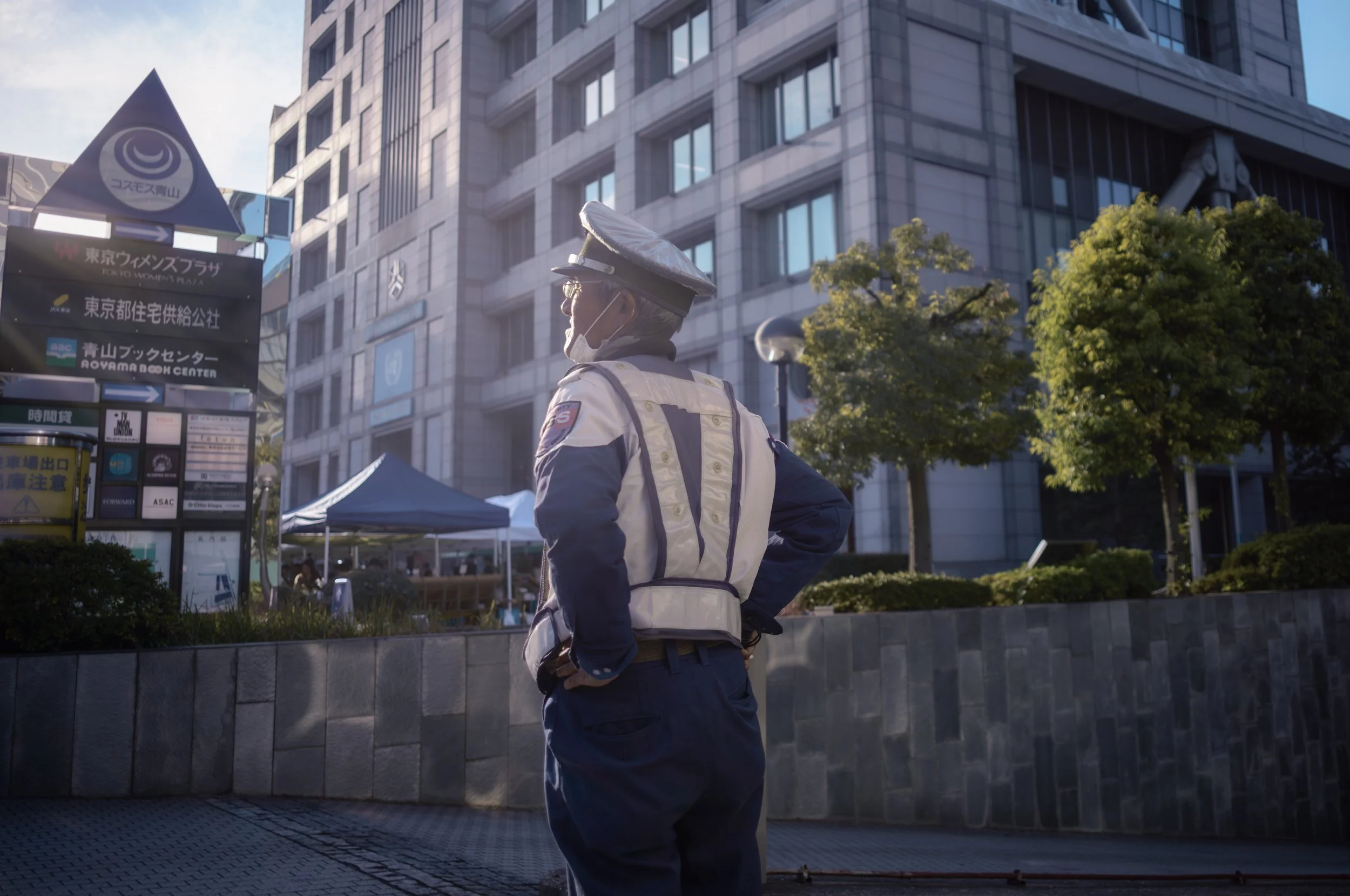 警察官が制服を着用し、マスクをつけている。建物と木々が背景に写っている都市の街角風景。