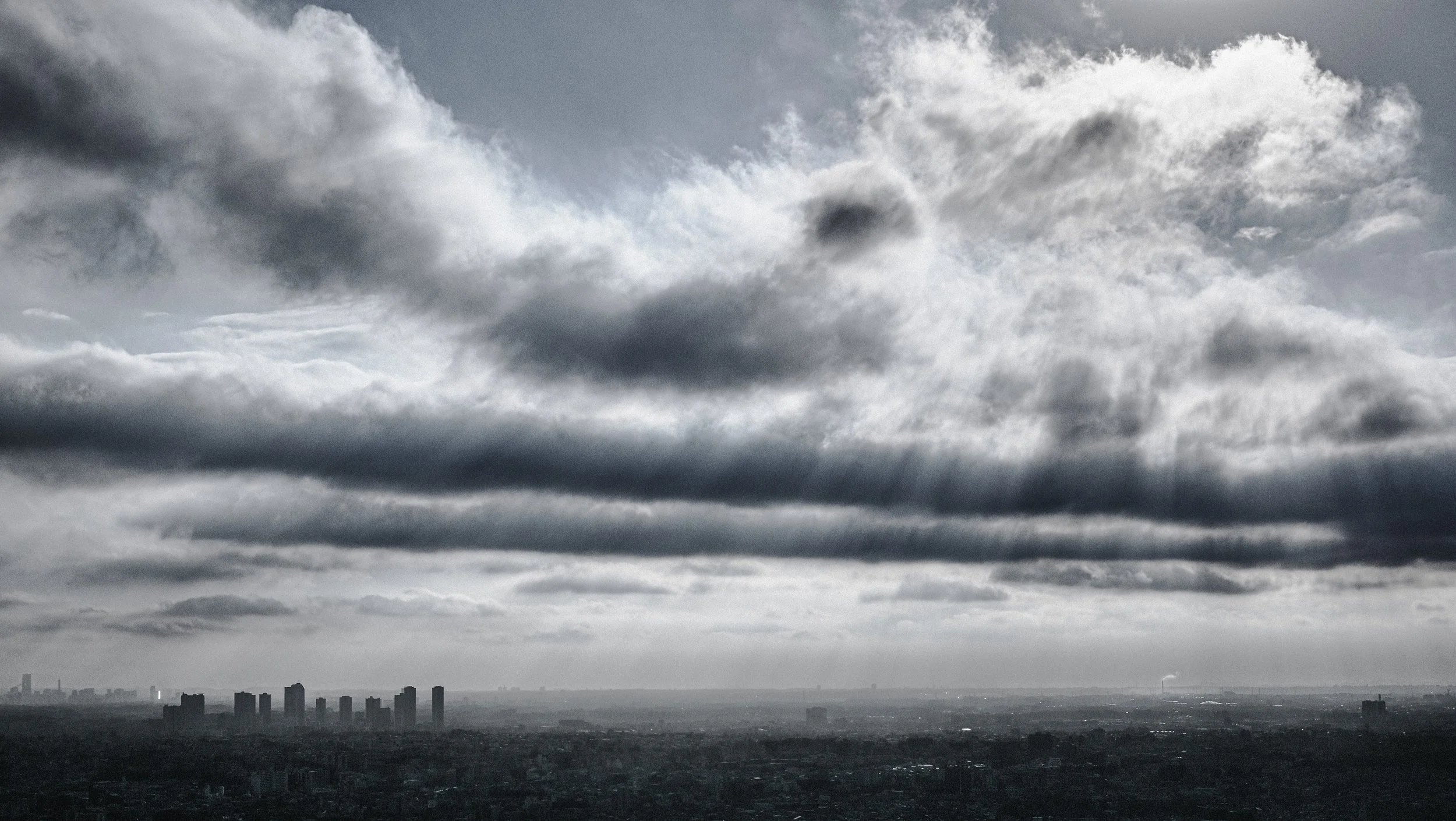灰色の厚い雲が空に広がり、都市のシルエットが下に広がる風景。
