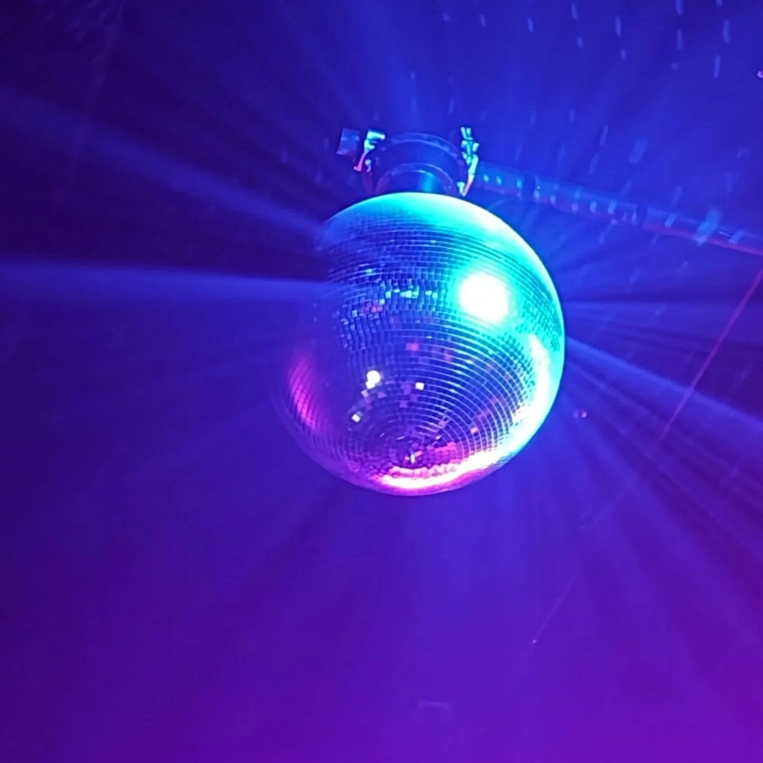 A disco ball reflecting light, creating a pattern of dots on the dark surrounding surface and a piece of fabric or paper underneath it.