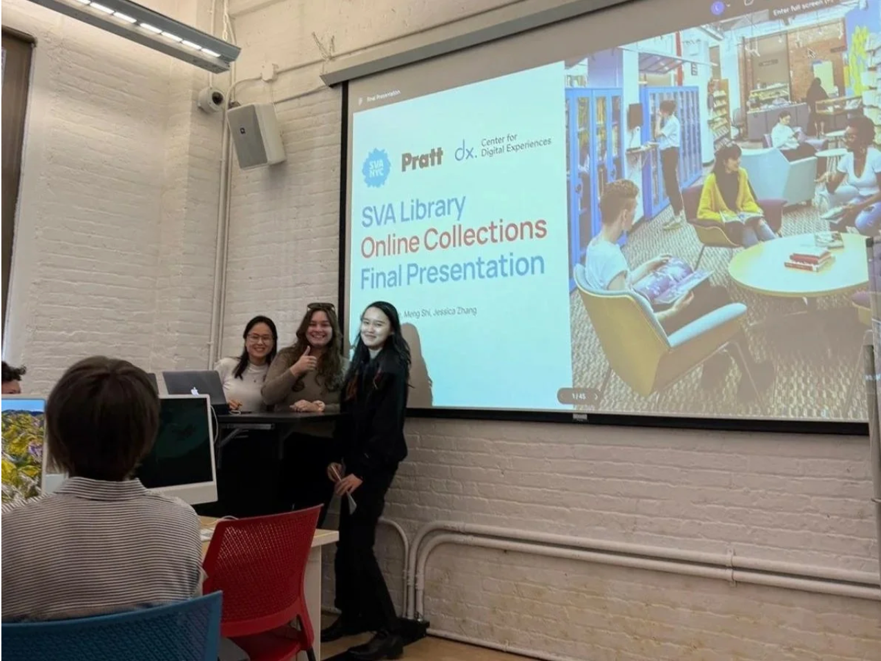 Three women standing on a stage in front of a large presentation screen, smiling and posing for a photo, with an audience member in the foreground, at a presentation titled 'SVA Library Online Collections Final Presentation'.