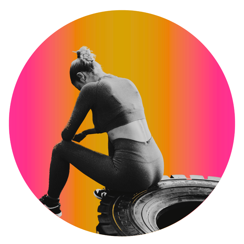 Woman rests after workout and sits on large tire, depicting the feeling of overworking in the gym and feeling disconnected.