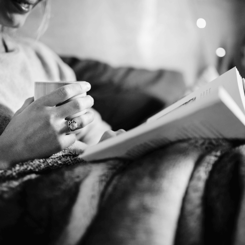 Woman relaxing on couch reading with a mug for Lüsha Method Gather book club