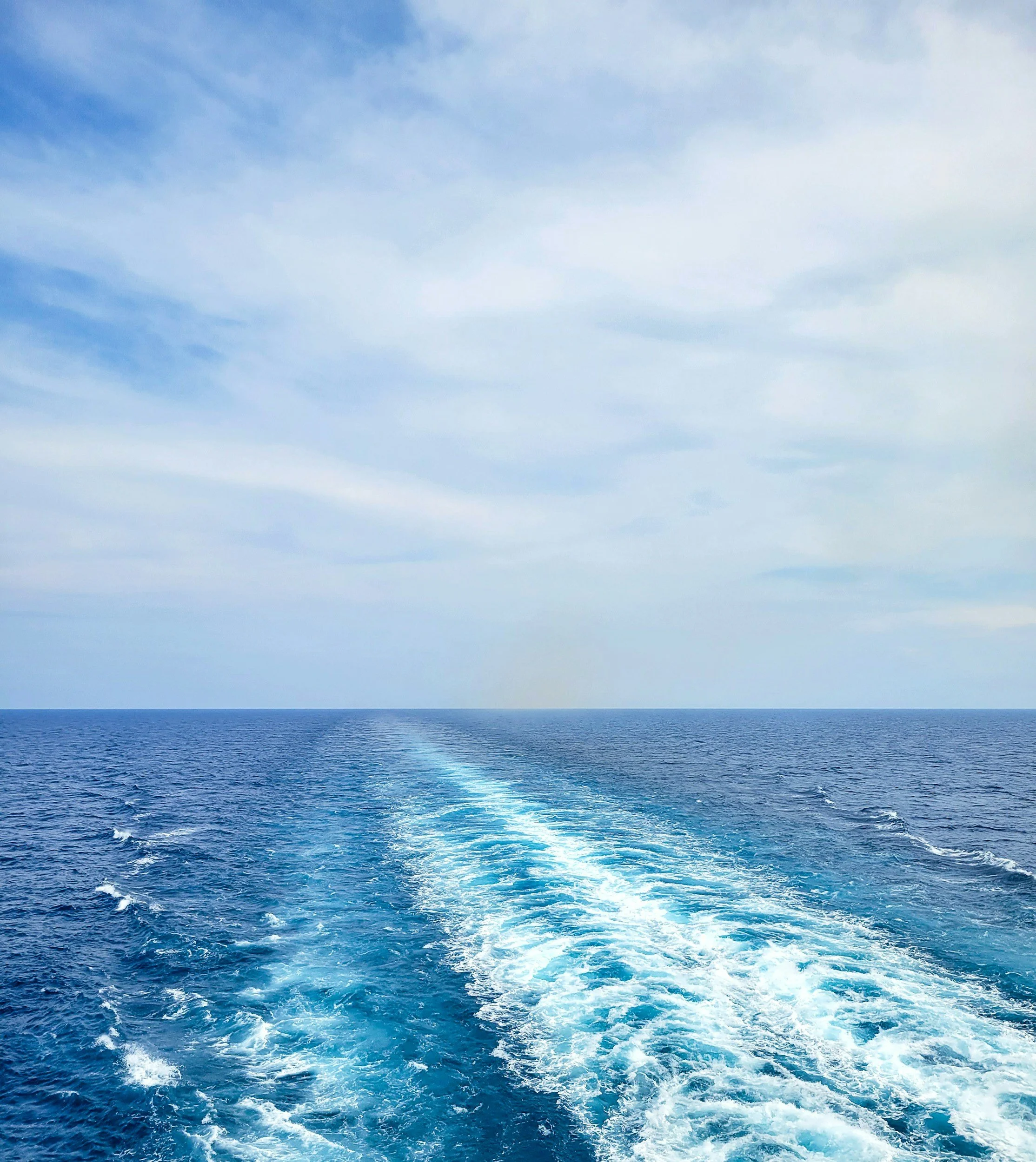 View of the ocean with a boat's wake and partly cloudy sky