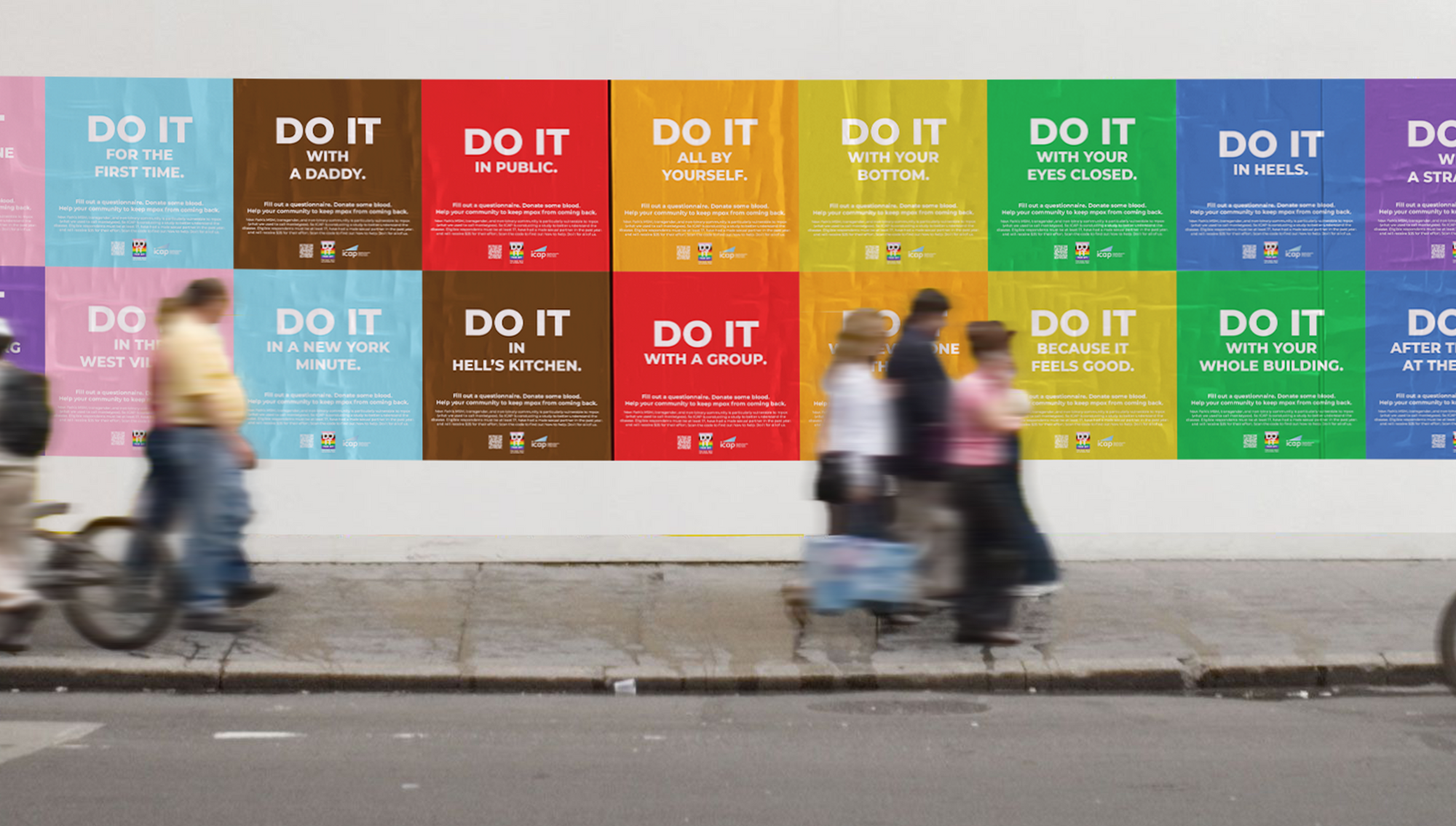 A wall with colorful posters displaying a series of 'Do It' messages in various colors and phrases, with blurred pedestrians walking past on a city sidewalk.