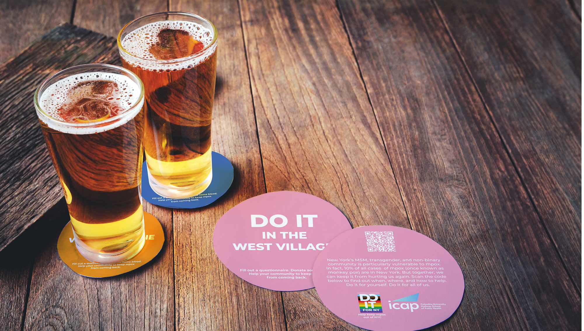Two glasses of amber beer on wooden table with circular posters promoting the importance of vaccination and community health, including a QR code and message about mumps.