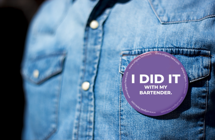 Person wearing a denim shirt with a purple button badge that reads 'I DID IT WITH MY BARTENDER.'