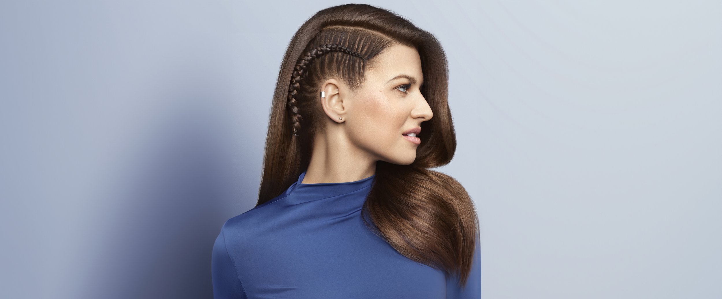 Profile of a woman with long braided hairstyle on the side, wearing a blue top, against a gradient background.