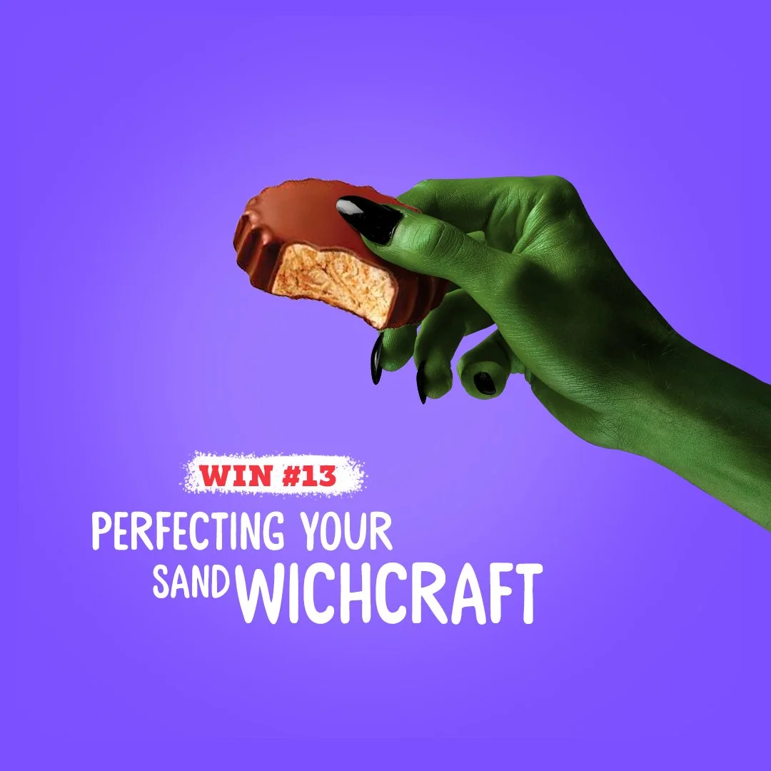 A hand painted green holding a partially eaten chocolate-covered wafer biscuit against a purple background. Text reads 'Win #13 Perfecting Your Sandwich Wichcraft'.
