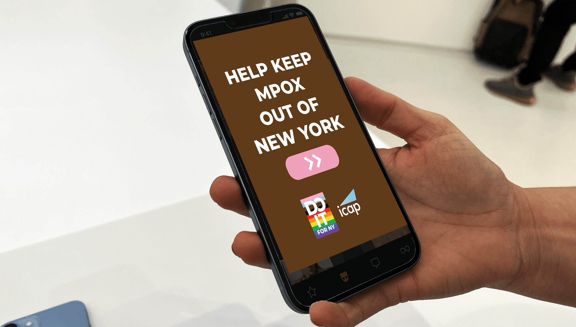 Hand holding a smartphone displaying a message to help keep MPPX out of New York, with logos of DC Black Pride, It Gets Better NY, and Icap at the bottom of the screen.