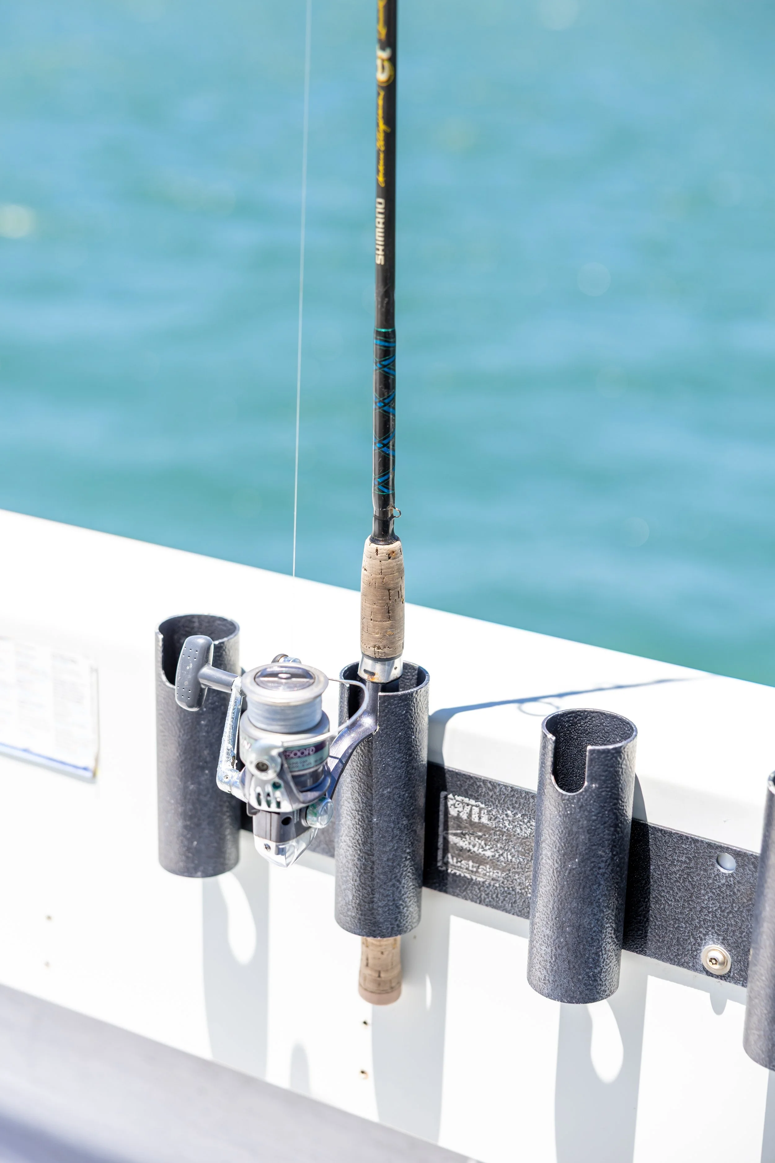 Day Tripper BBQ Pontoon Boat - Lake Macquarie. Fishing rod and reel secured in a holder on a boat with water in the background.
