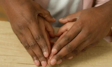 Two pairs of hands gently holding each other, resting on a wooden surface.