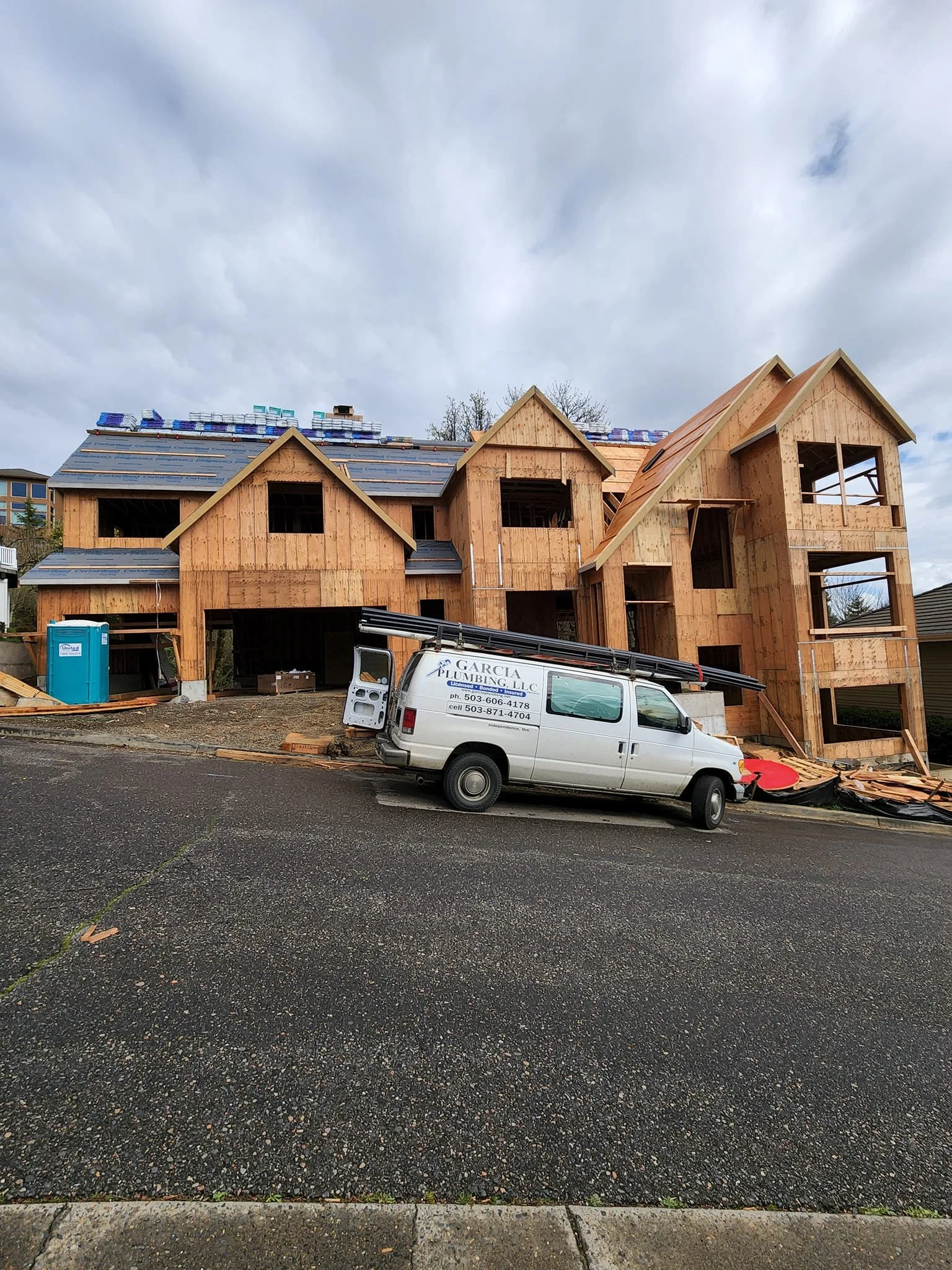 A house under construction with wooden framing and a black asphalt roof, a white Garcia Plumbing company van parked in front.