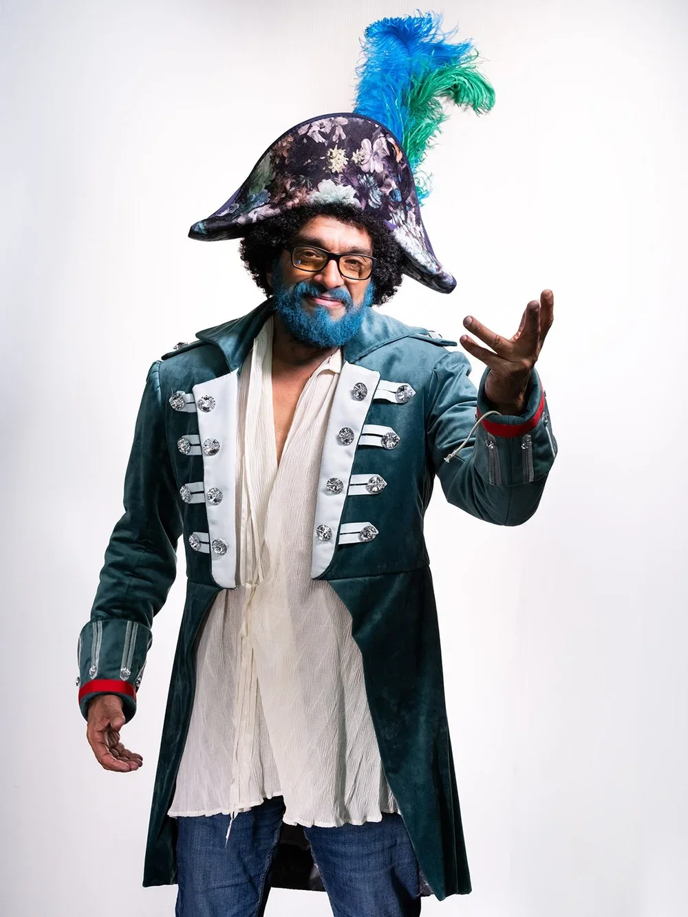 A man with blue hair and beard wearing a elaborate costume, including a large decorated hat with feathers, bold coat with decorative buttons, standing against a white background.