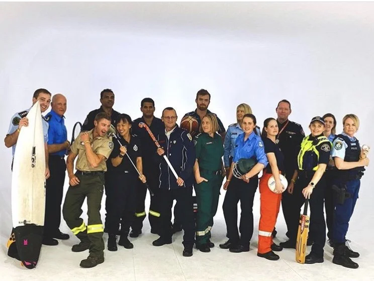 Group of emergency responders, including police officers, firefighters, paramedics, and other rescue personnel, standing together against a plain white background.