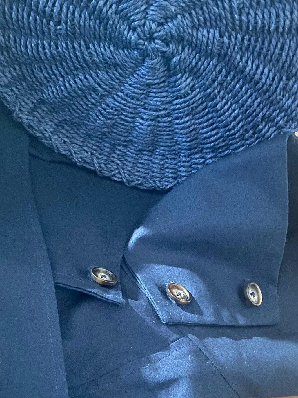 Close crop of a navy woven straw bag resting against a tailored navy coat, showing tonal colour matching between contrasting textures in a coordinated outfit