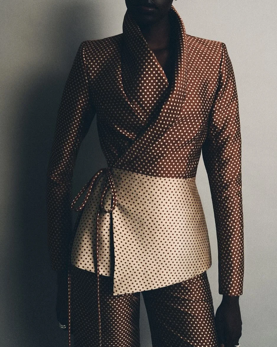 Person in a tailored asymmetric side-tie blazer with clashing dot prints, presenting a polished look that quietly subverts conventional dress codes.
