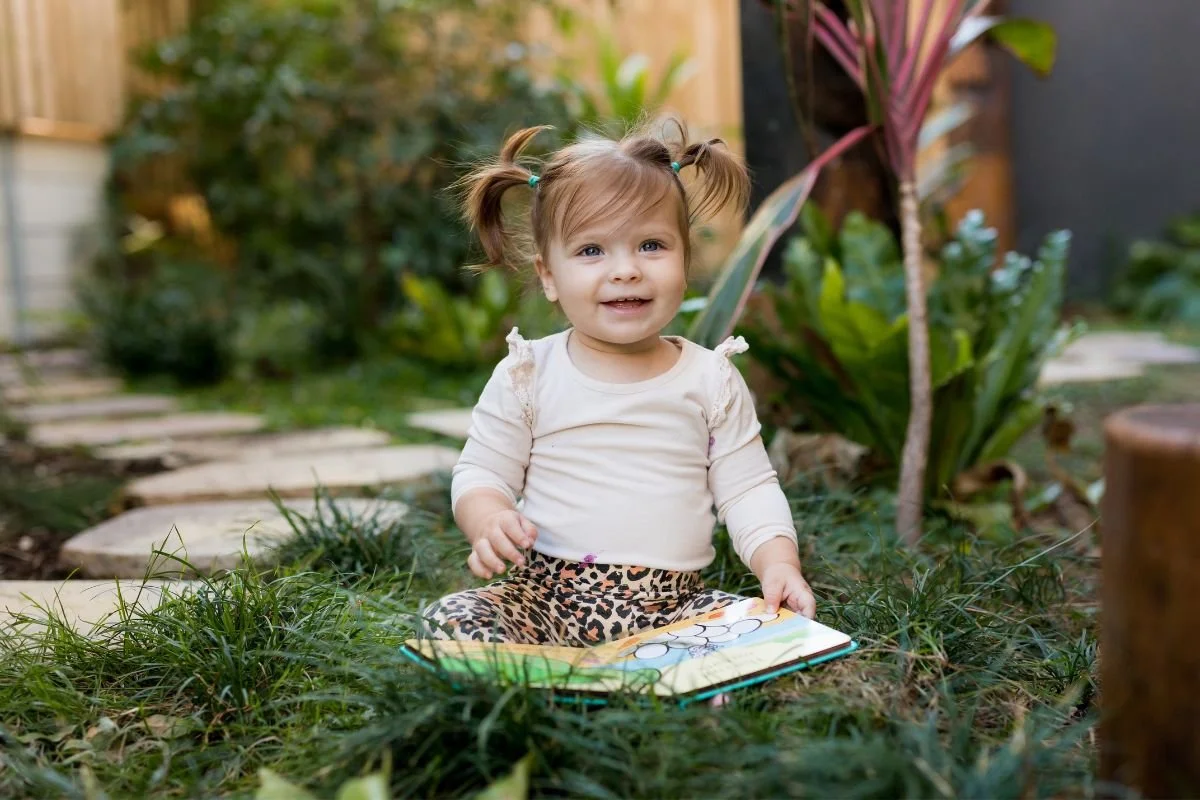 Toddler sitting in grassy area for a portrait with preschool photographer