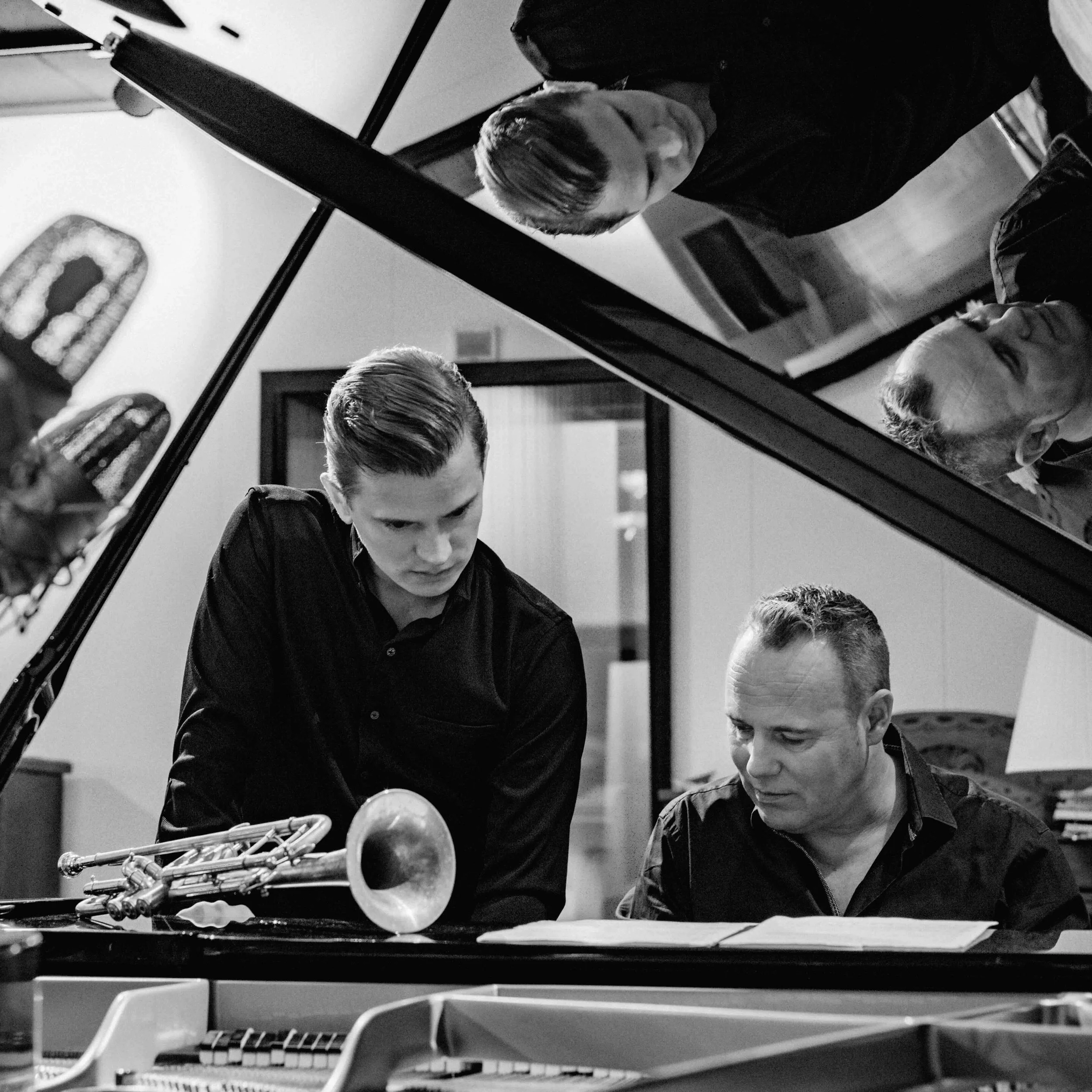 A young man with dark hair playing the piano, with sheet music on the stand and a trumpet lying on the piano. The scene is in a room with artwork on the wall reminiscent of a 50's Blue Note recording session
