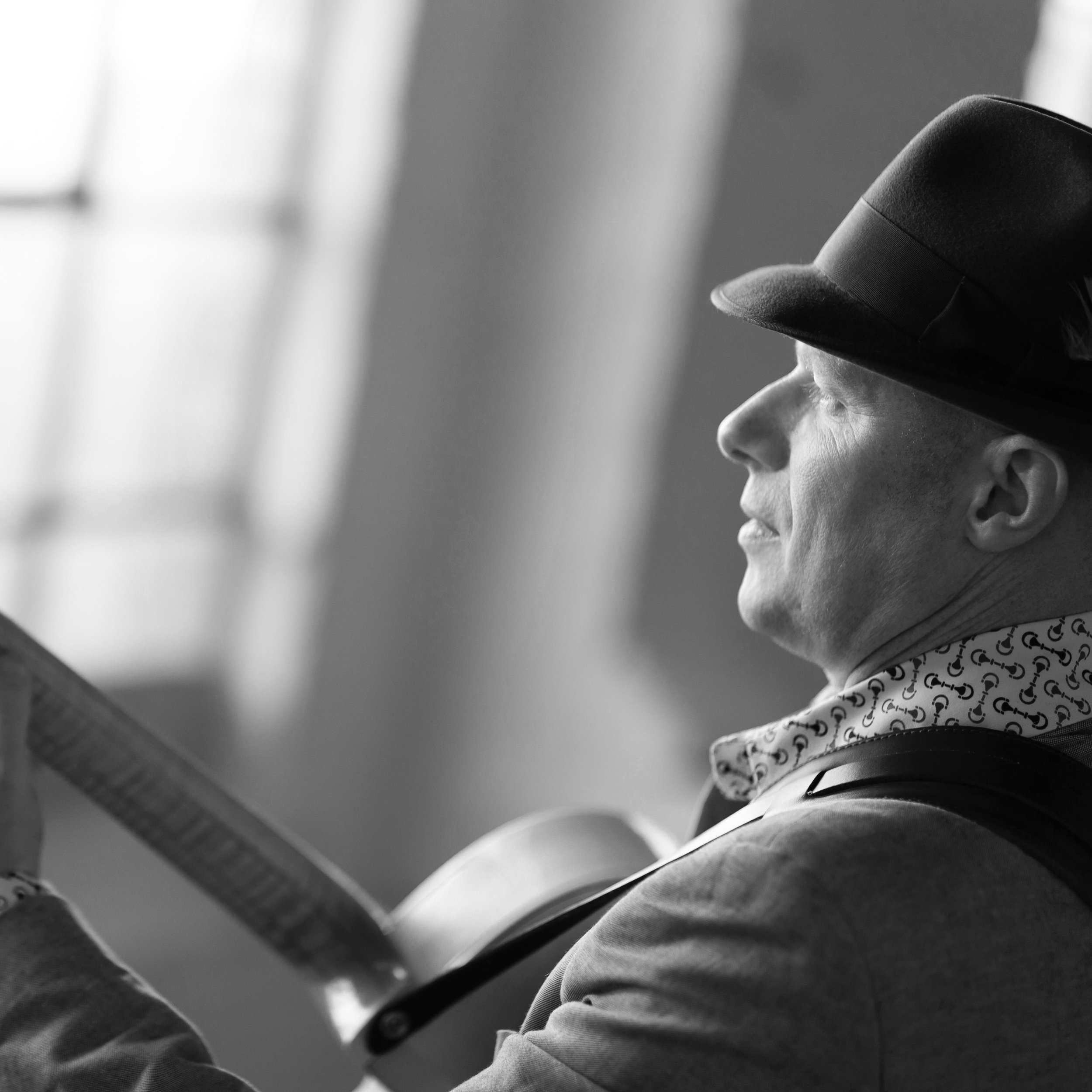 A person wearing a hat with a decorative band is sitting, looking down, in a black-and-white photo.