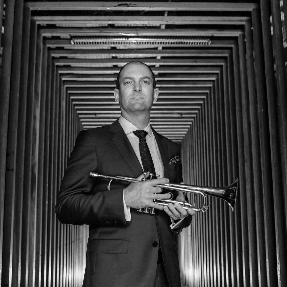 Man in suit holding trumpet in a tunnel of metal rods.