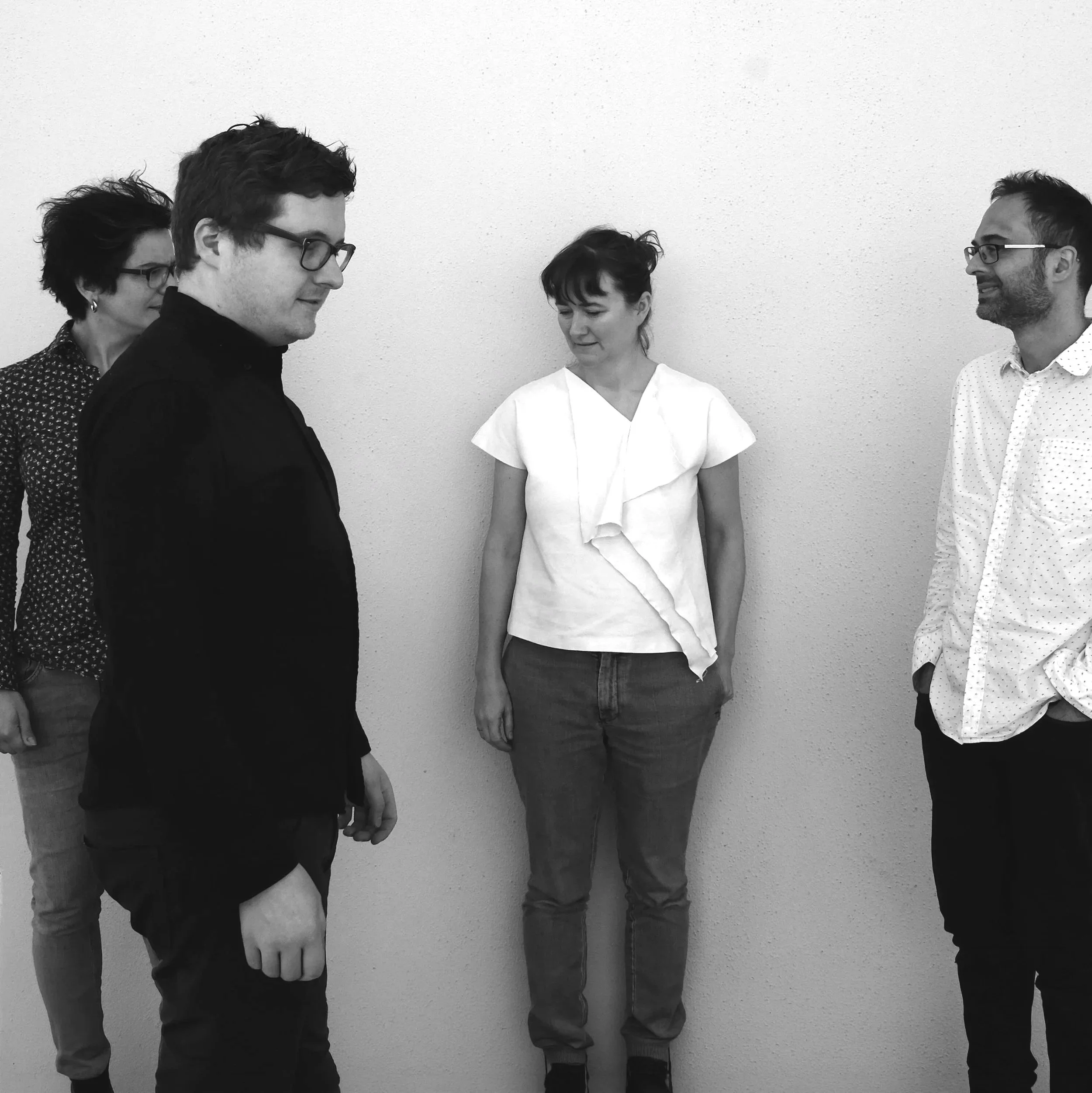 Four diverse individuals standing and smiling in a line against a plain wall.
