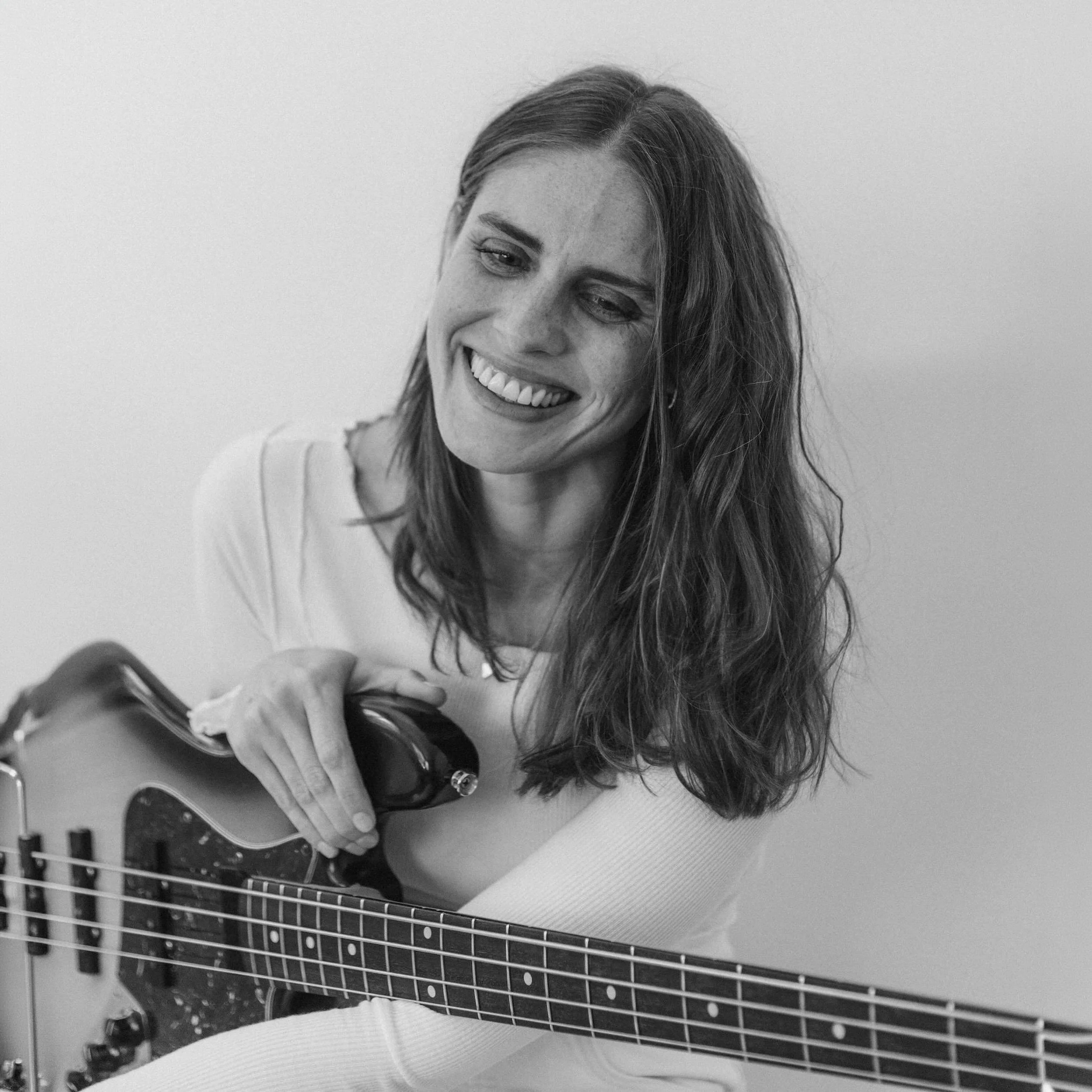 A woman with long hair smiling and holding an electric guitar.