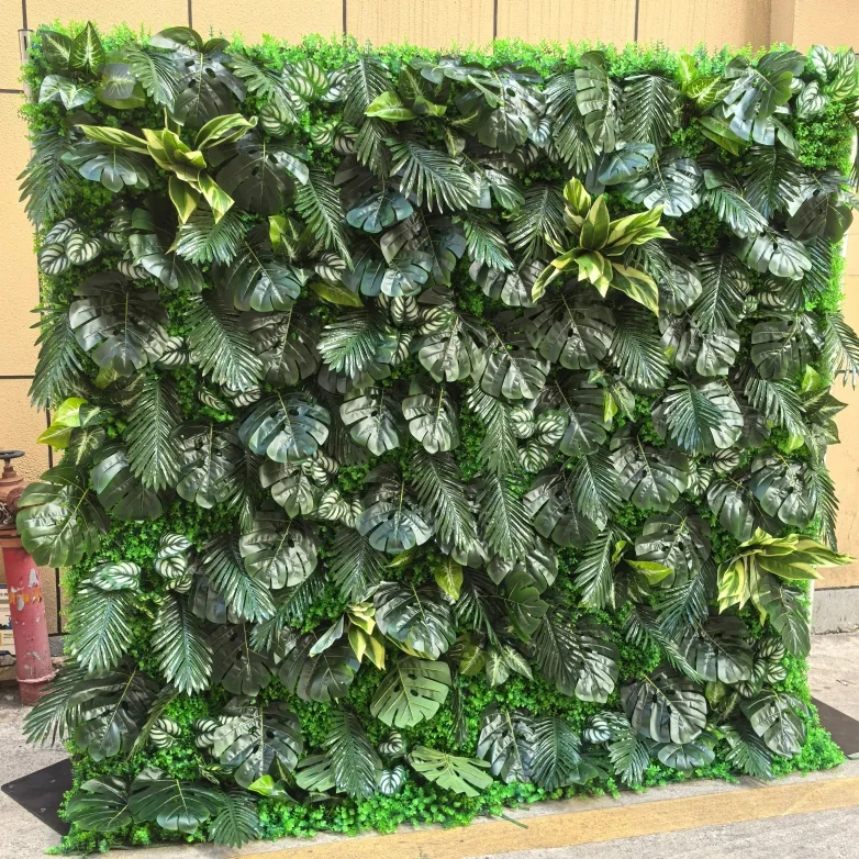 A decorative wall made of various green plants and leaves, including monstera and fern leaves, arranged in a grid pattern.