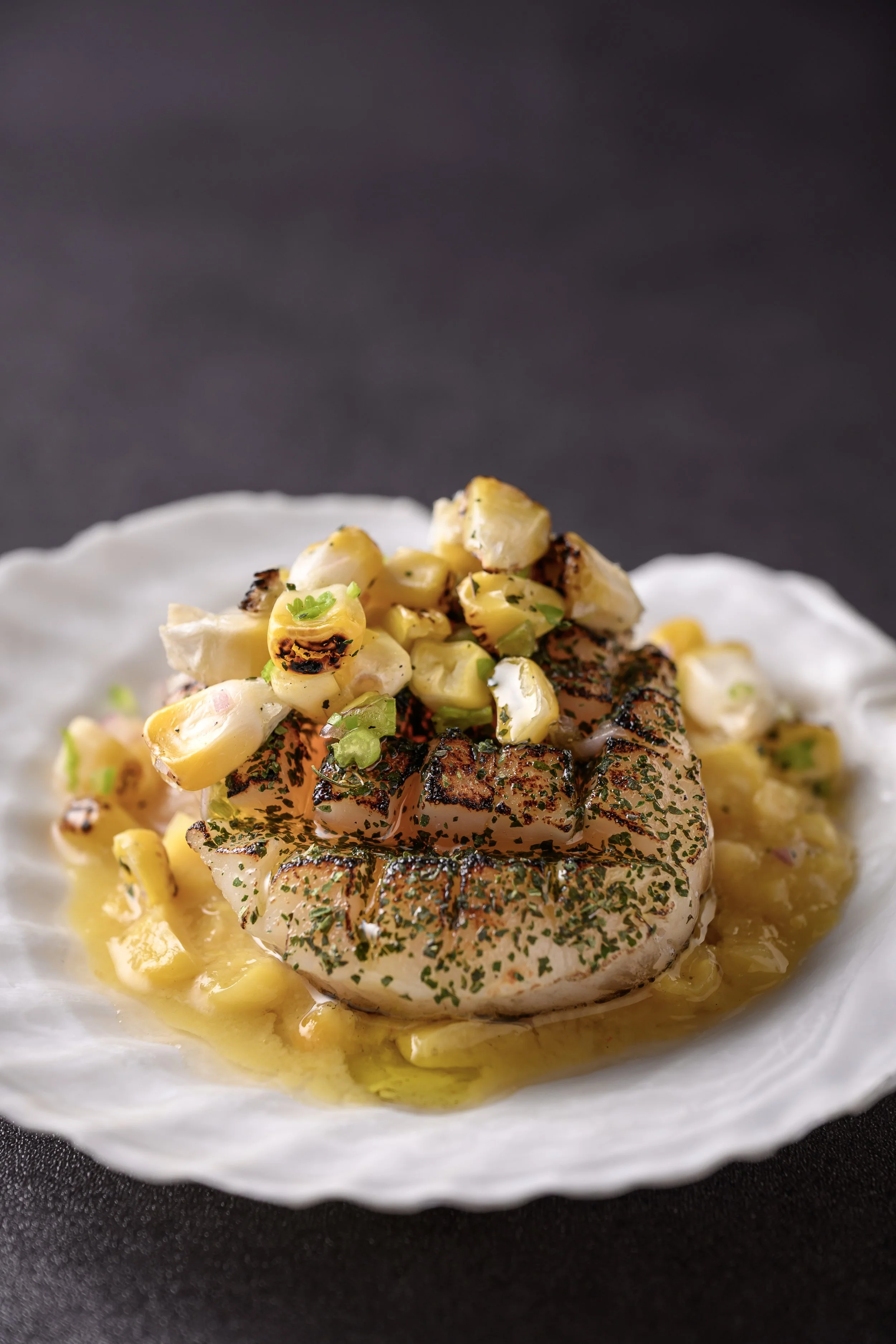Grilled salmon steak topped with diced roasted garlic, green herbs, and a lemon butter sauce on a white plate.