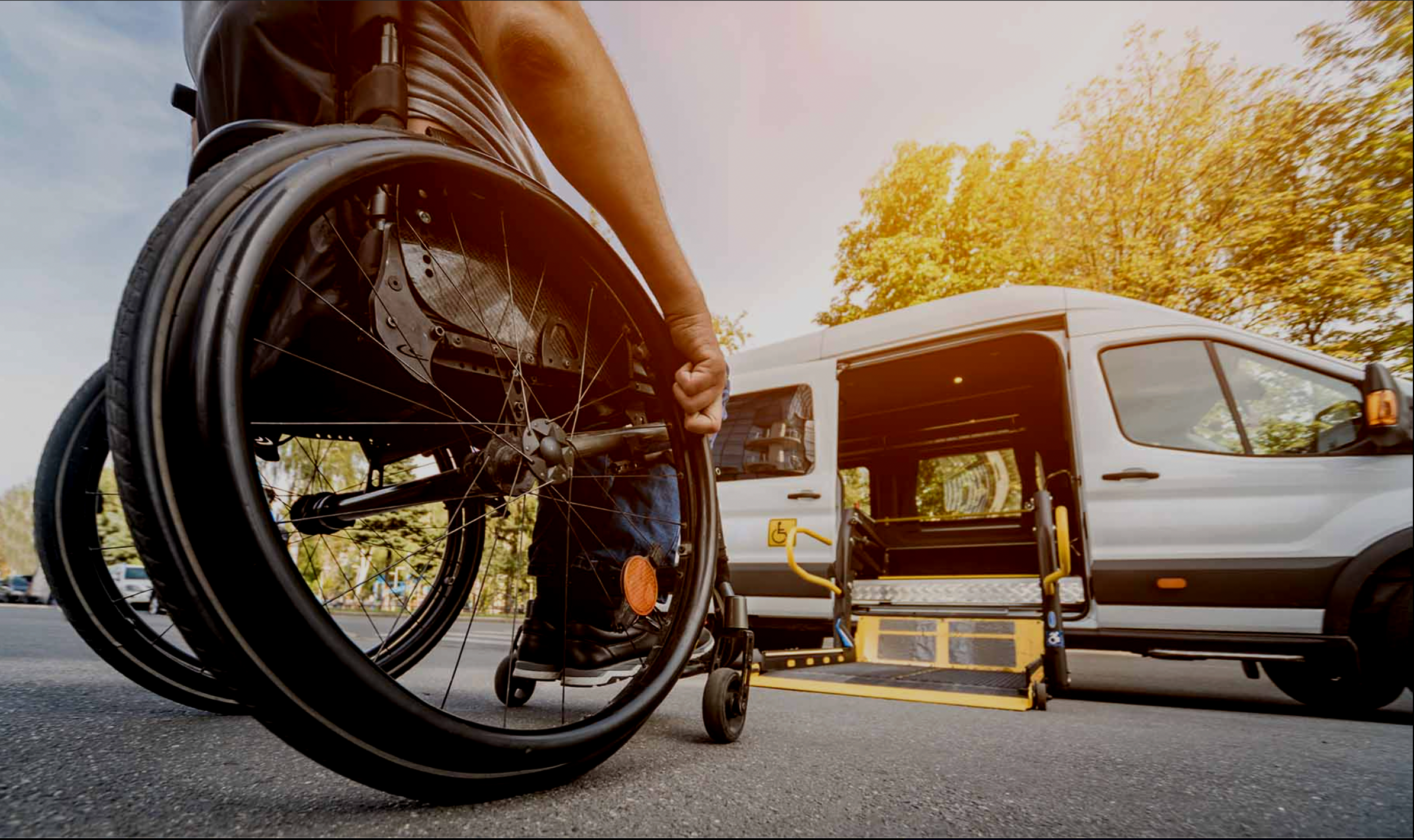 Person in a wheelchair boarding a vehicle designed for wheelchair accessibility with a ramp outside on a sunny day.