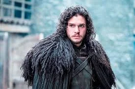 A man with long, curly dark hair wearing a black fur-lined cloak outdoors.