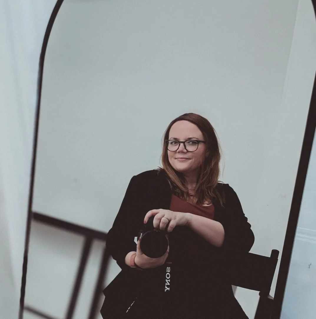 Frau mit Brille macht ein Selfie vor einem Spiegel, im Hintergrund eine weiße Wand.