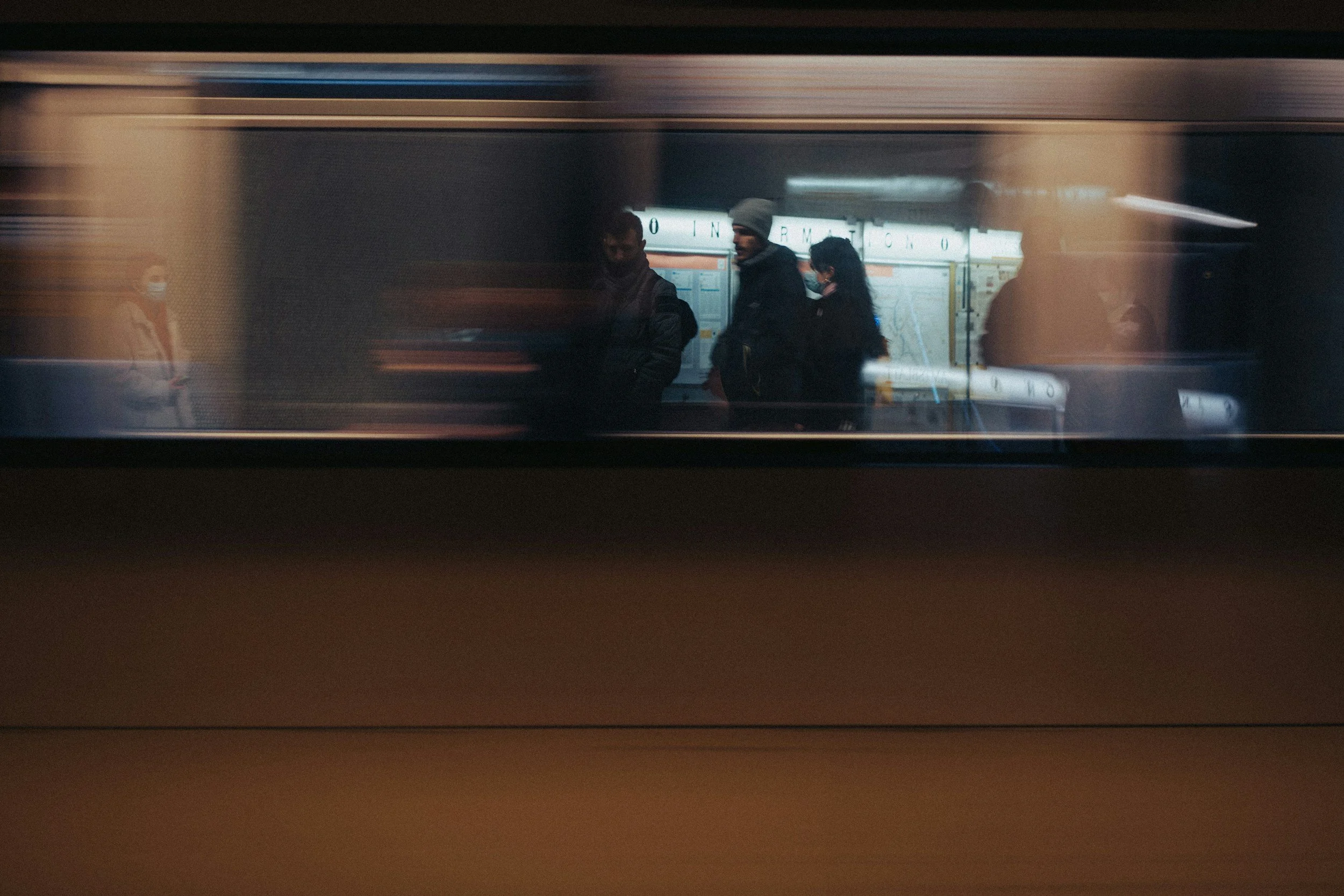 People waiting at a subway station, seen through the window of a moving train.